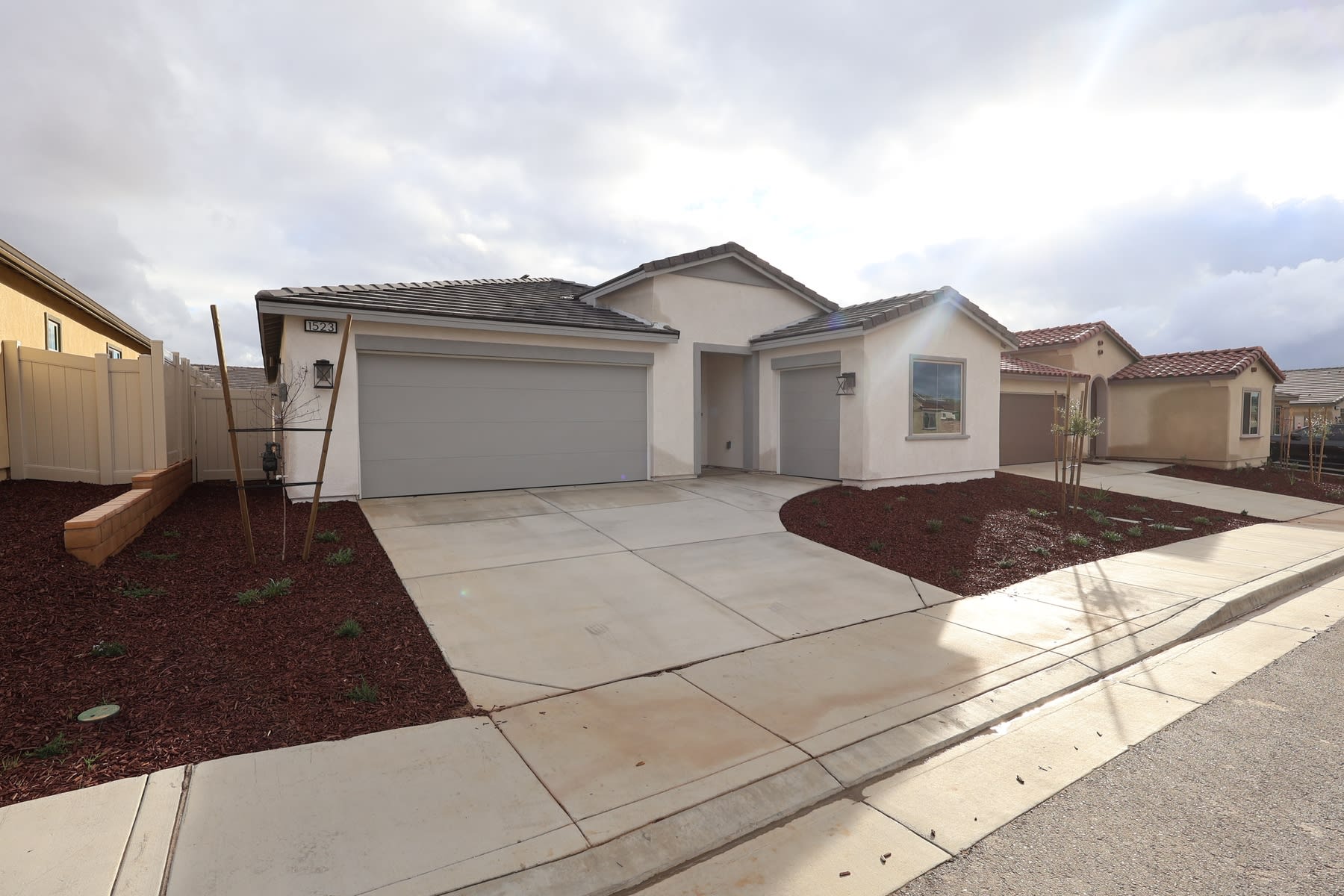 A single-story residential home with a garage, surrounded by a paved driveway and landscaped yard with mulch and plants in the foreground.