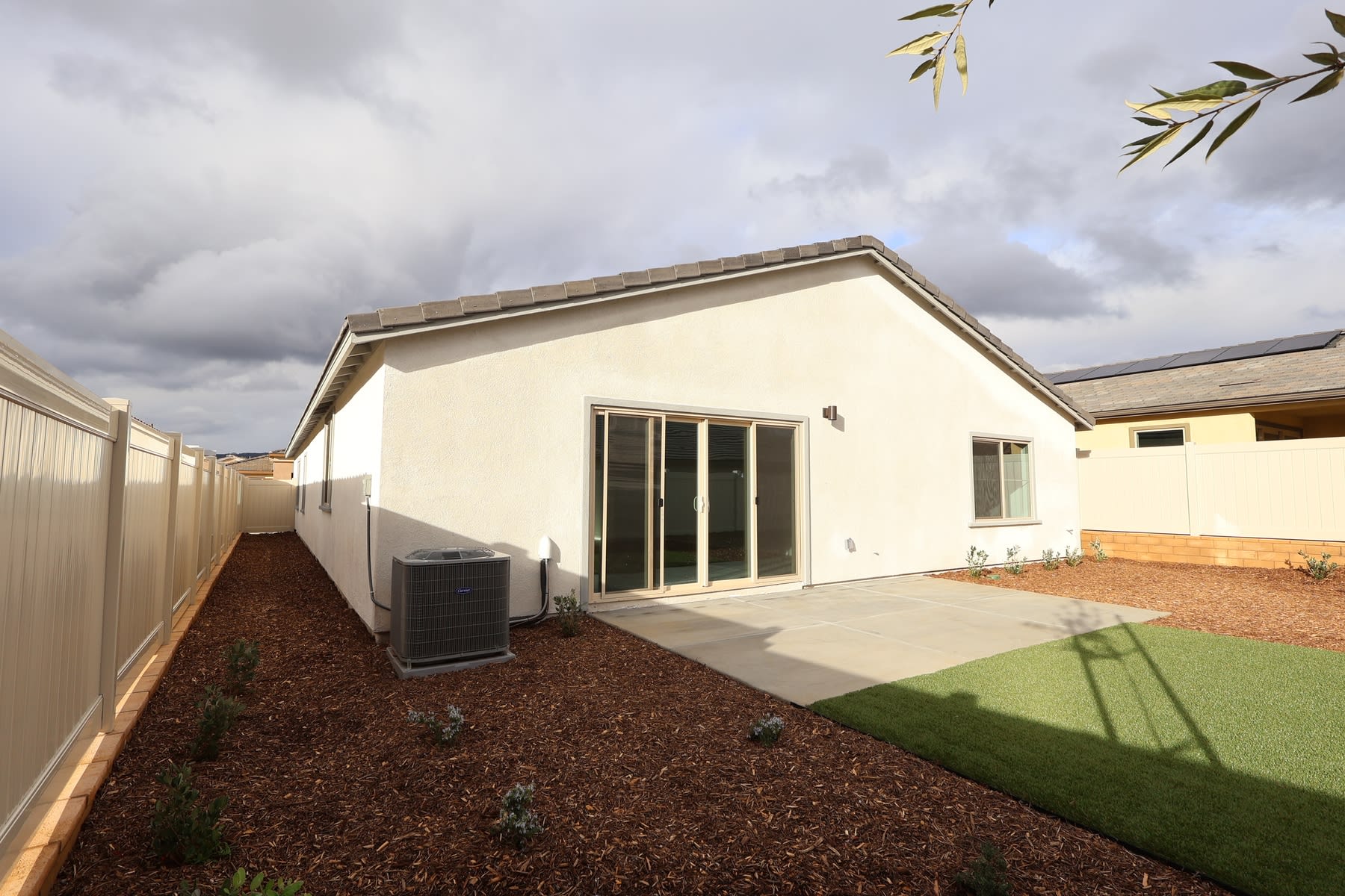 A single-story house with a patio and a well-maintained yard, surrounded by a fence and landscaping elements such as mulch and grass.