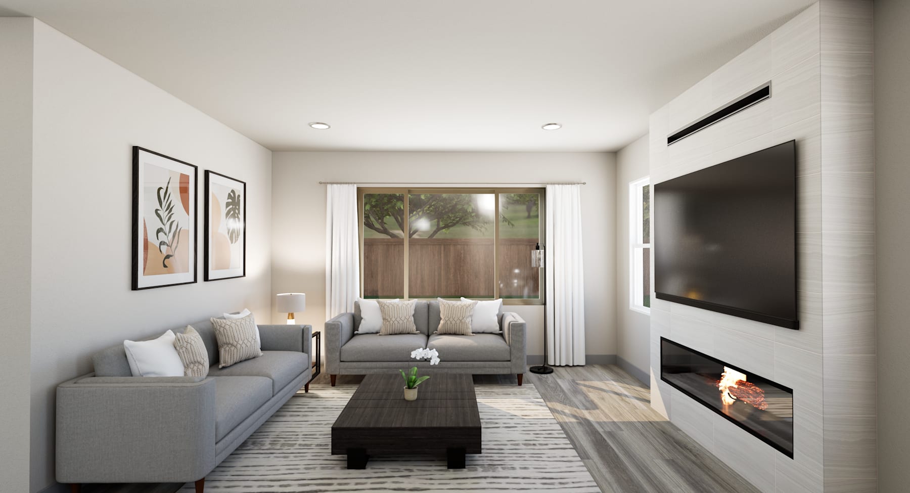 A cozy and modern living room with a gray sofa, a coffee table, and a fireplace, surrounded by framed artwork on the walls and a view of the outdoors through a window.