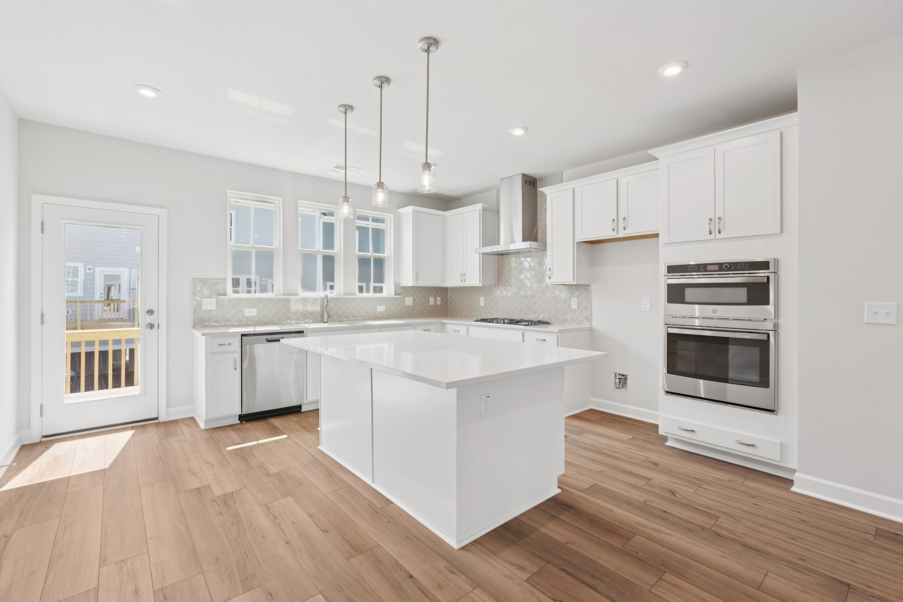 A modern, bright kitchen with white cabinets, stainless steel appliances, and hardwood floors, featuring a central island and pendant lighting.