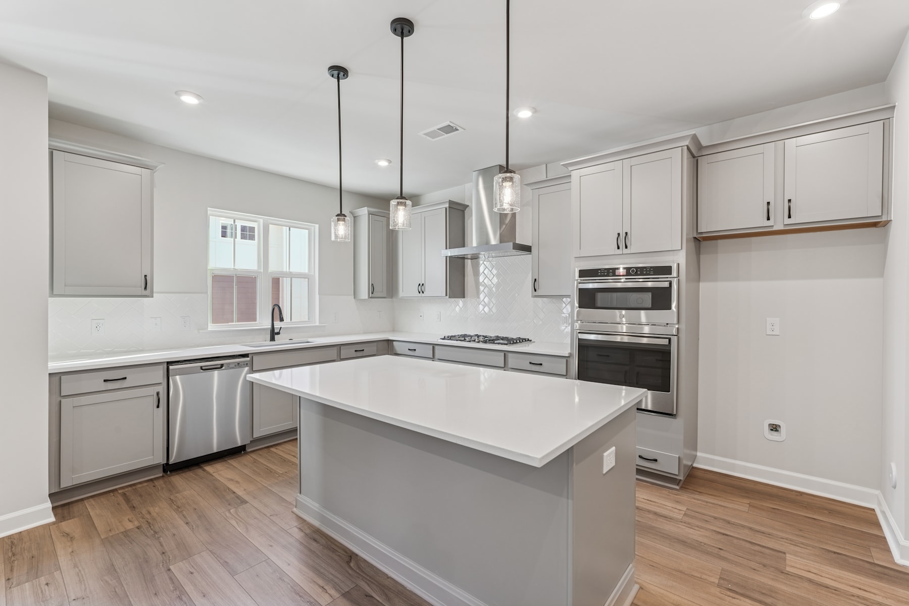 A modern, well-lit kitchen with white cabinets, a central island, and hardwood floors.