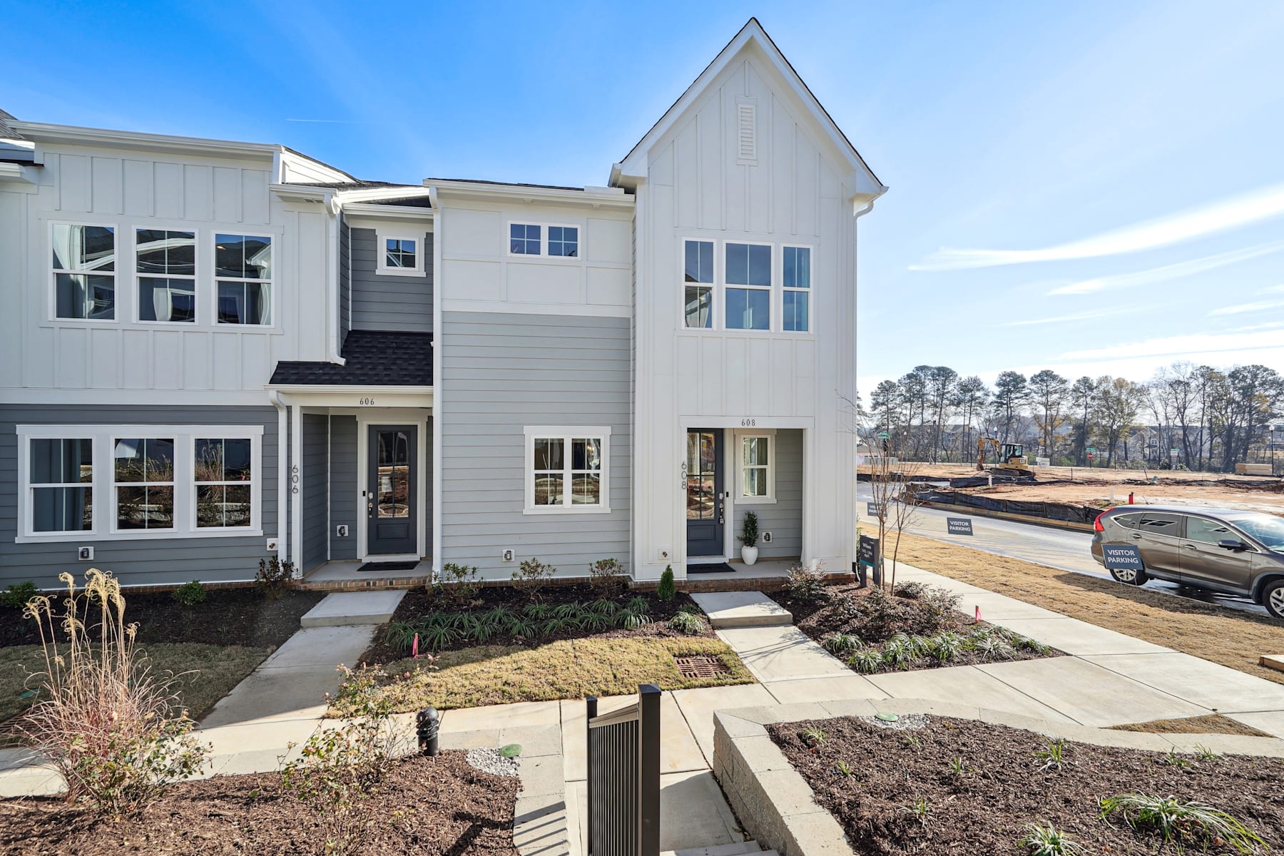 A modern, multi-story townhouse with a landscaped front yard and a clear blue sky in the background.