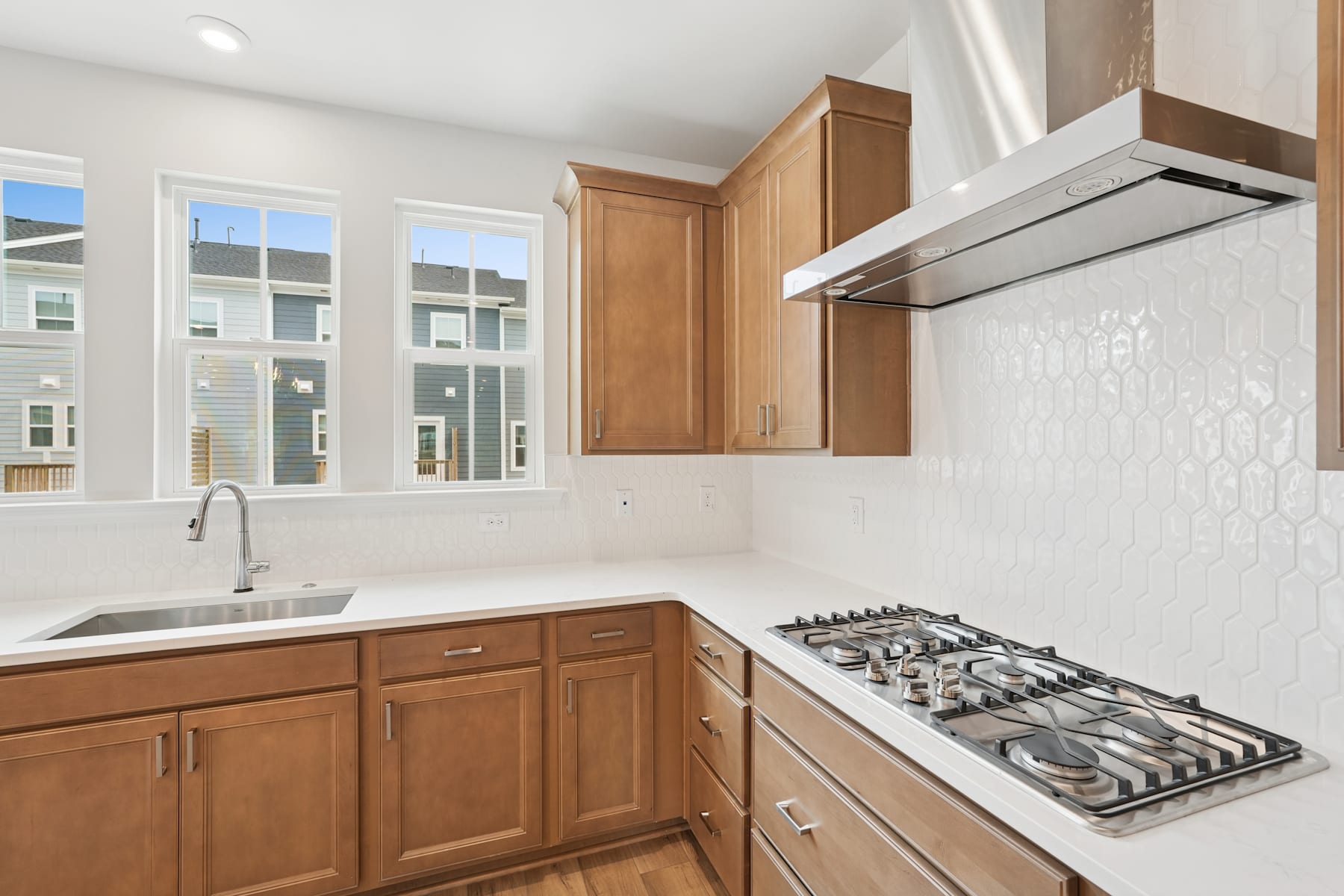 A modern kitchen with wooden cabinets, a gas stove, and large windows providing ample natural light.