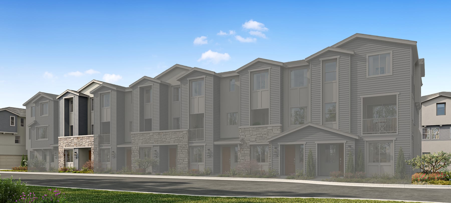 A row of modern, multi-story townhouses with gray siding and stone accents, set against a clear blue sky with fluffy white clouds.