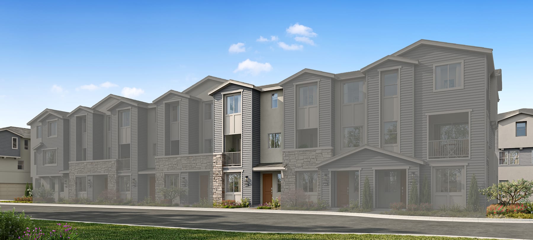 A row of modern, multi-story townhouses with gray siding and stone accents, set against a clear blue sky with fluffy white clouds.