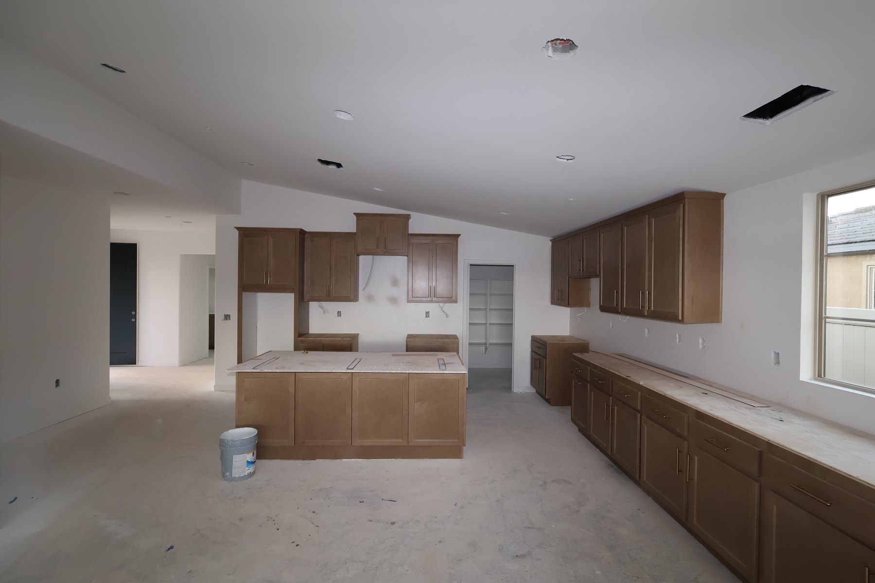 An empty kitchen with wooden cabinets and a central island, with a window visible in the background.