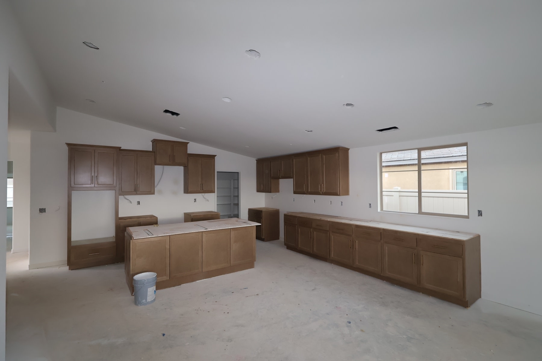 An empty kitchen with wooden cabinets, a white countertop, and a tiled floor, with a window providing natural light.