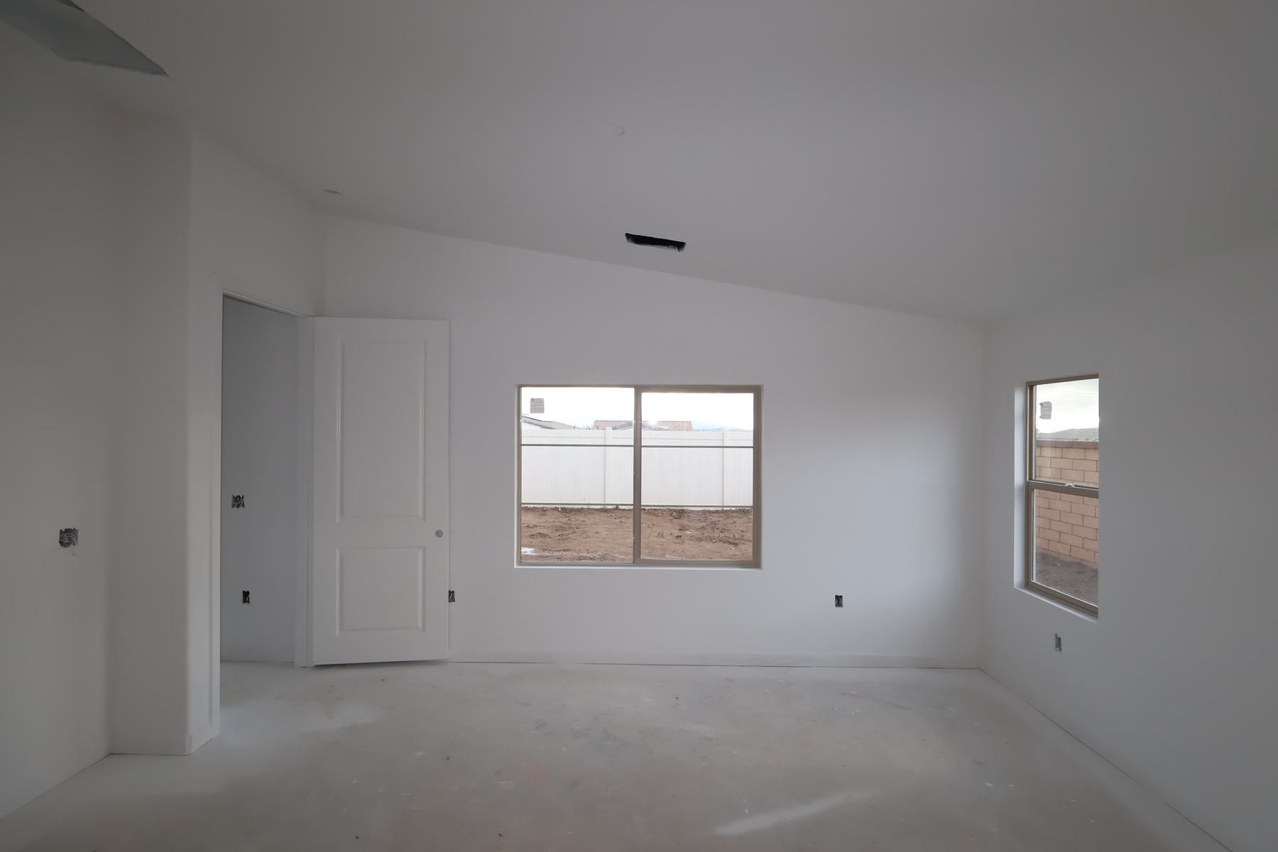 A minimalist, empty room with white walls, a closed door, and several windows providing natural light.