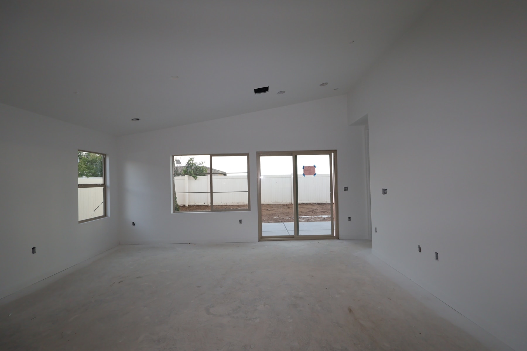 An empty, unfinished room with white walls, a sliding glass door, and a window, with a concrete floor visible.
