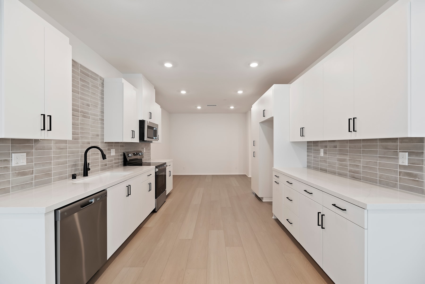 A modern, minimalist kitchen with white cabinets, gray tile backsplash, and hardwood floors, creating a clean and spacious atmosphere.