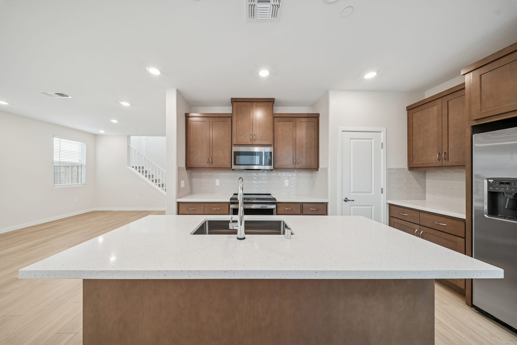 A modern, open-concept kitchen with wooden cabinets, white countertops, and stainless steel appliances, set against a bright and airy background.