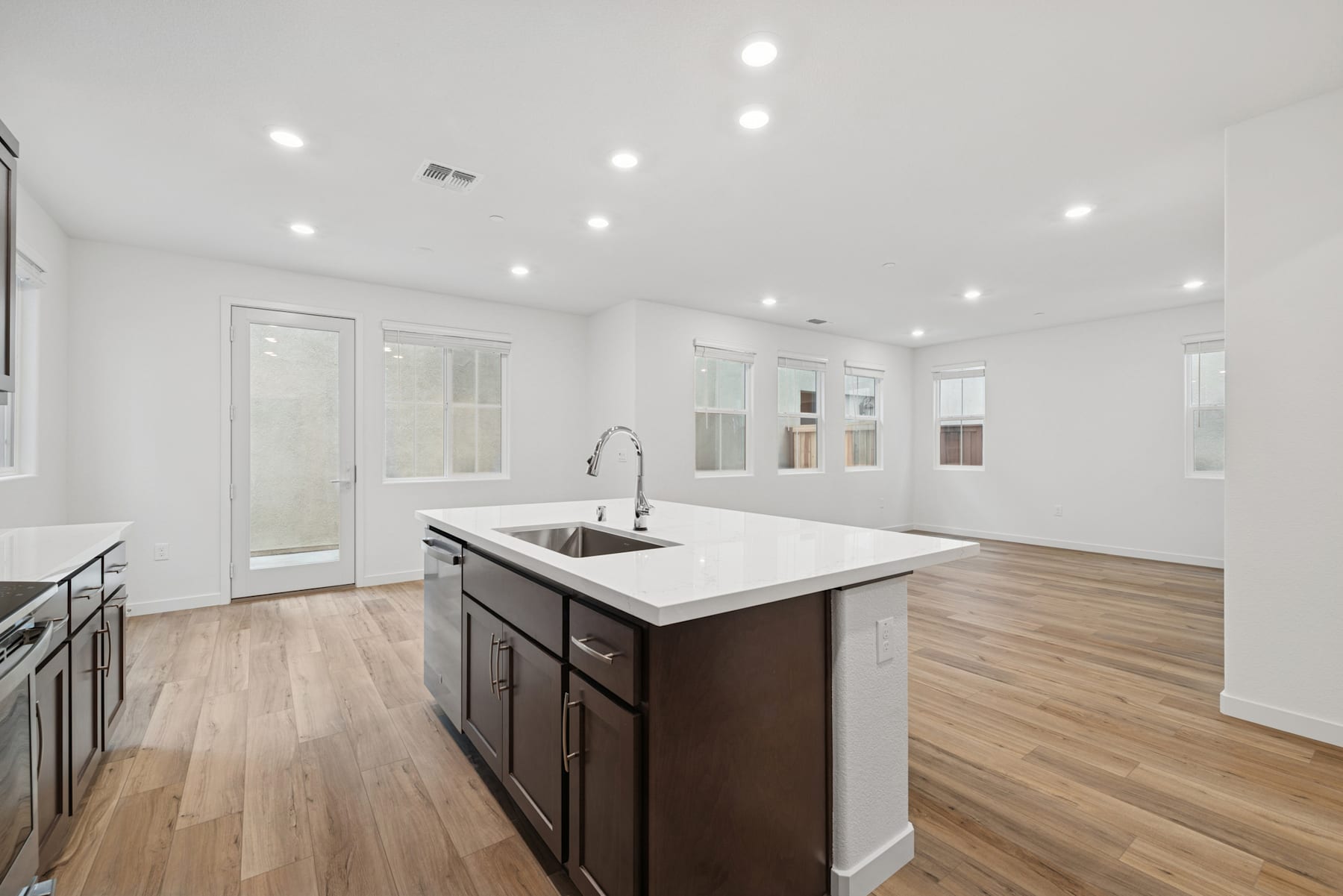 A modern, open-concept kitchen with a large island, dark cabinets, and hardwood floors, surrounded by bright, airy windows.