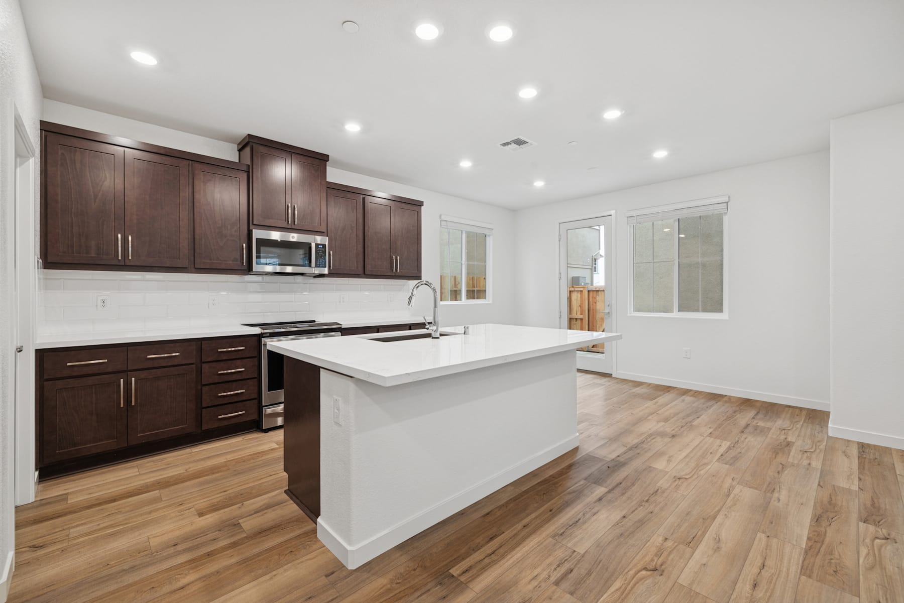 A modern, well-lit kitchen with dark wood cabinets, a white countertop island, and hardwood flooring.