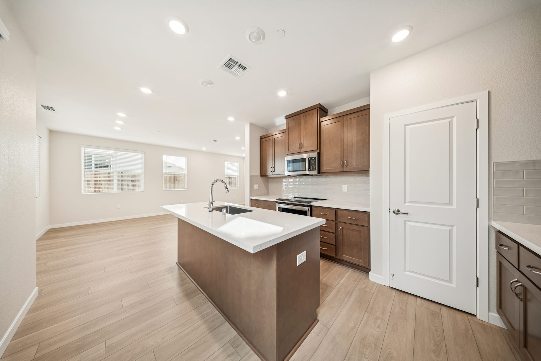 A modern, open-concept kitchen with light wood cabinets, a white countertop, and hardwood flooring, set against a bright and airy background.