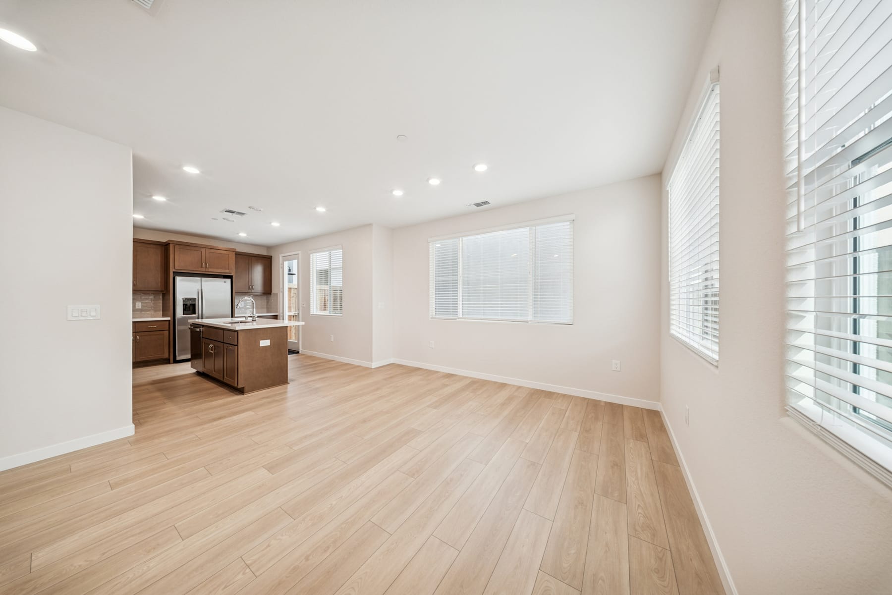 A spacious, well-lit room with hardwood floors, modern kitchen appliances, and large windows providing ample natural light.