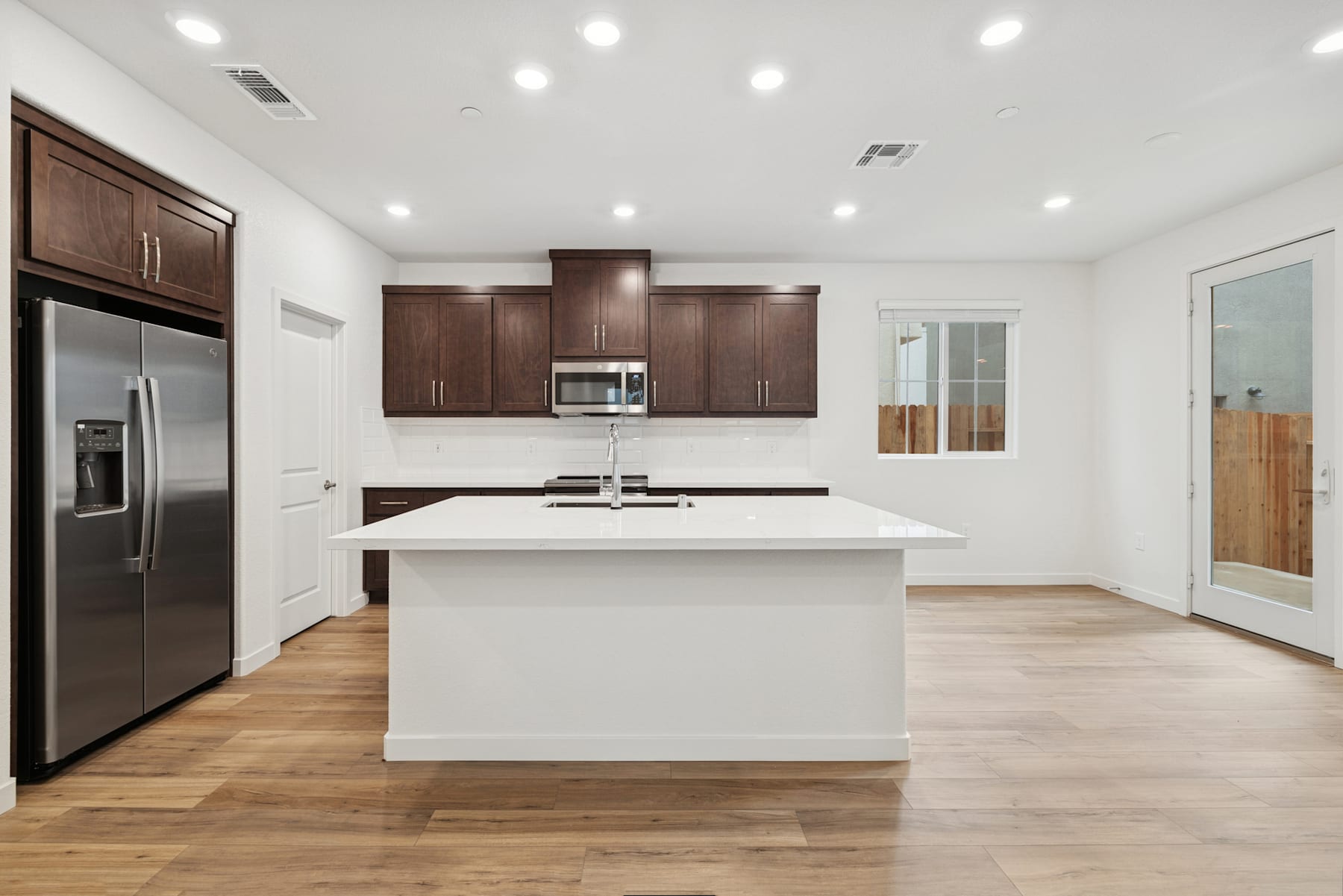 A modern, well-lit kitchen with dark wood cabinets, a white island countertop, and hardwood floors.