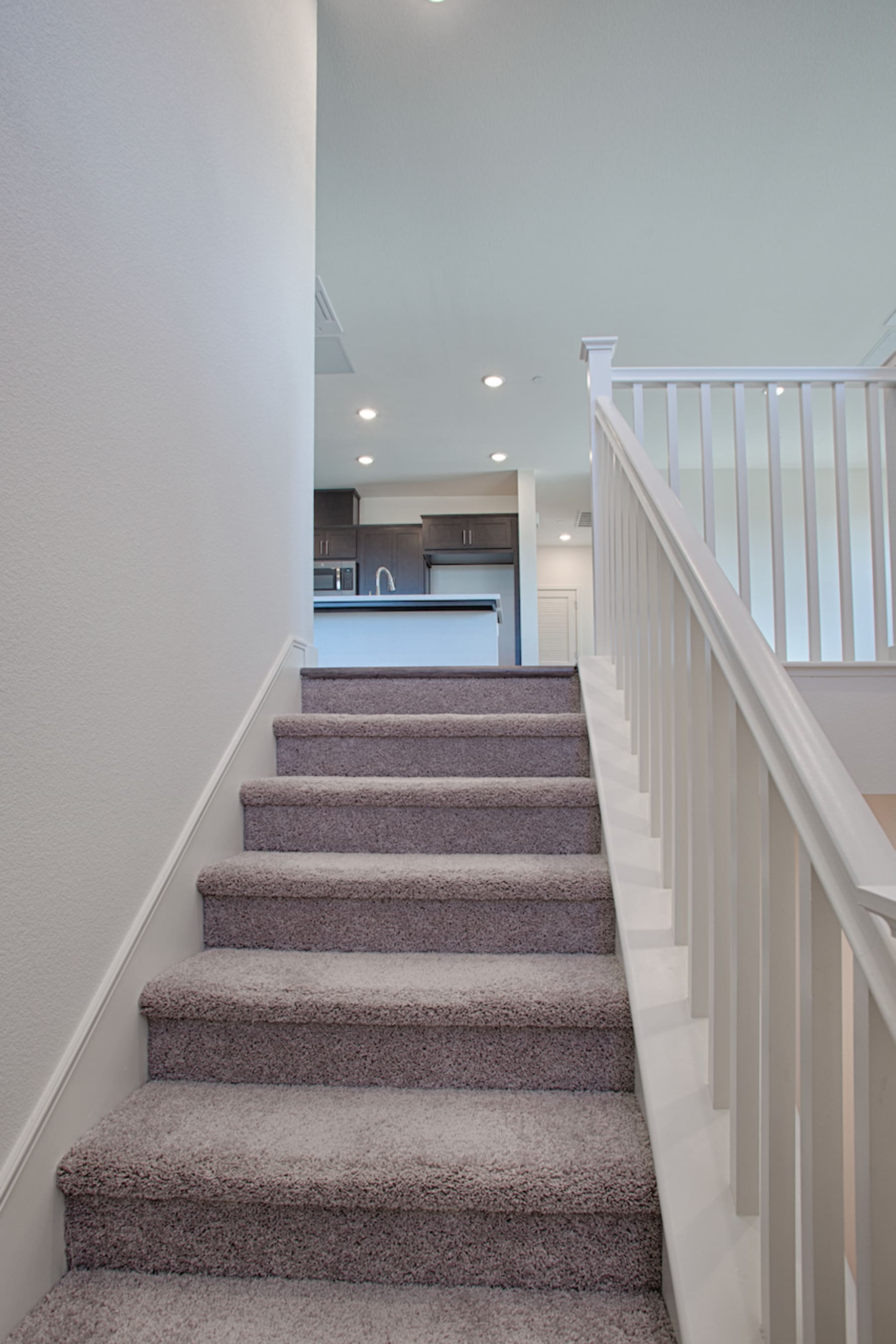 The image shows a staircase with white railings leading up to a kitchen area in the background.