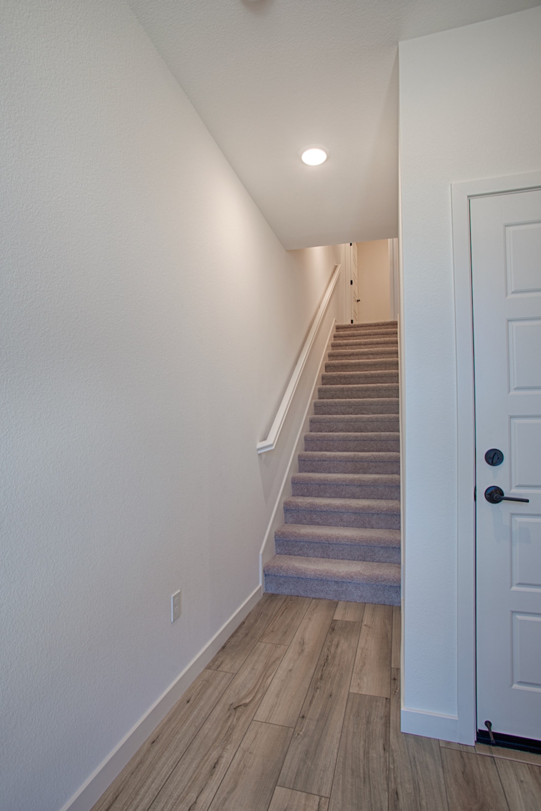 A staircase leading up to a second floor, with a white wall and a wooden floor visible in the foreground.