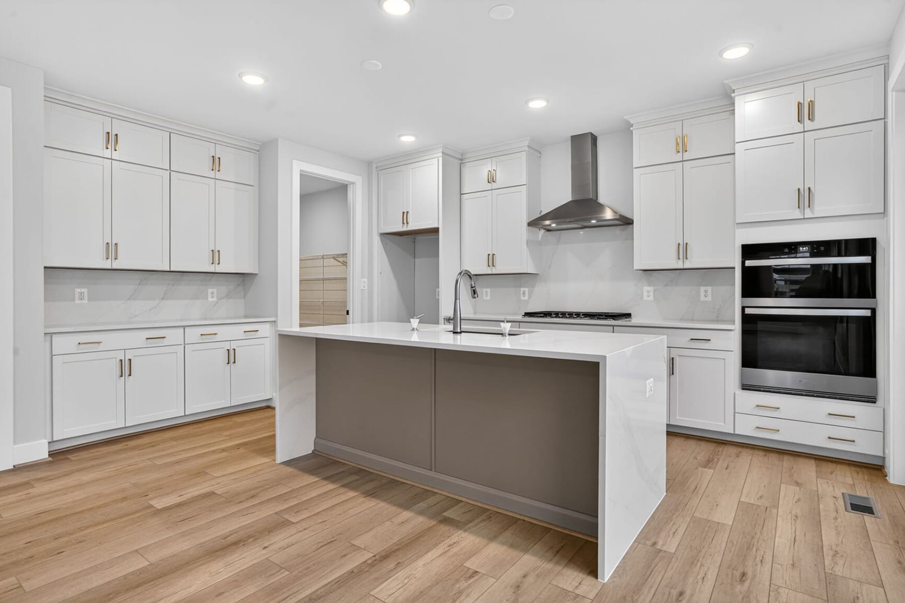A modern, well-lit kitchen with white cabinets, a central island, and hardwood floors.