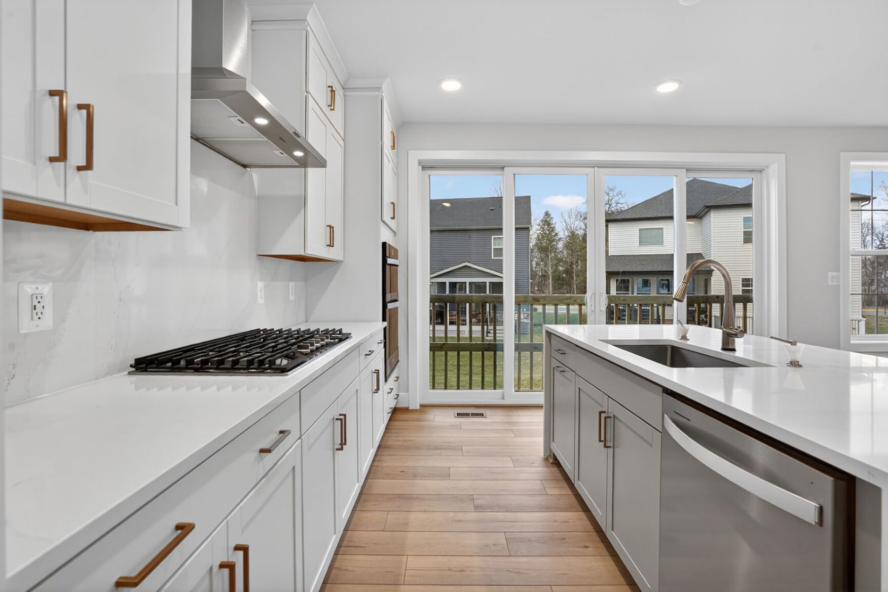 A modern, well-equipped kitchen with white cabinets, stainless steel appliances, and a view of a residential neighborhood through a large window.