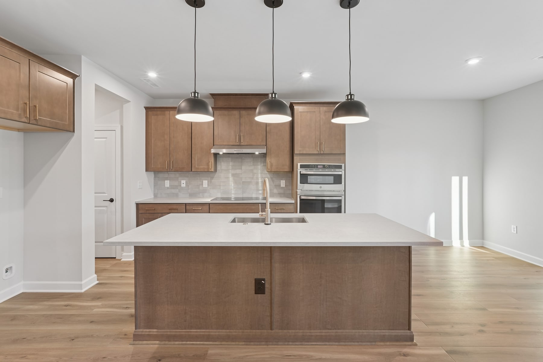 A modern, open-concept kitchen with light wood cabinetry, a large island with a white countertop, and pendant lighting fixtures hanging above.