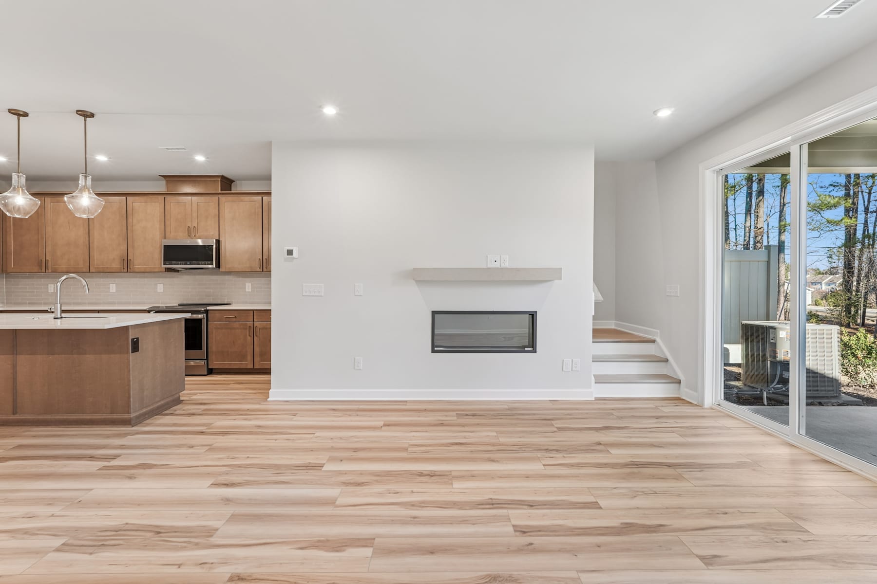A modern, open-concept living space with a kitchen, fireplace, and hardwood floors leading to a sliding glass door that provides access to an outdoor area.