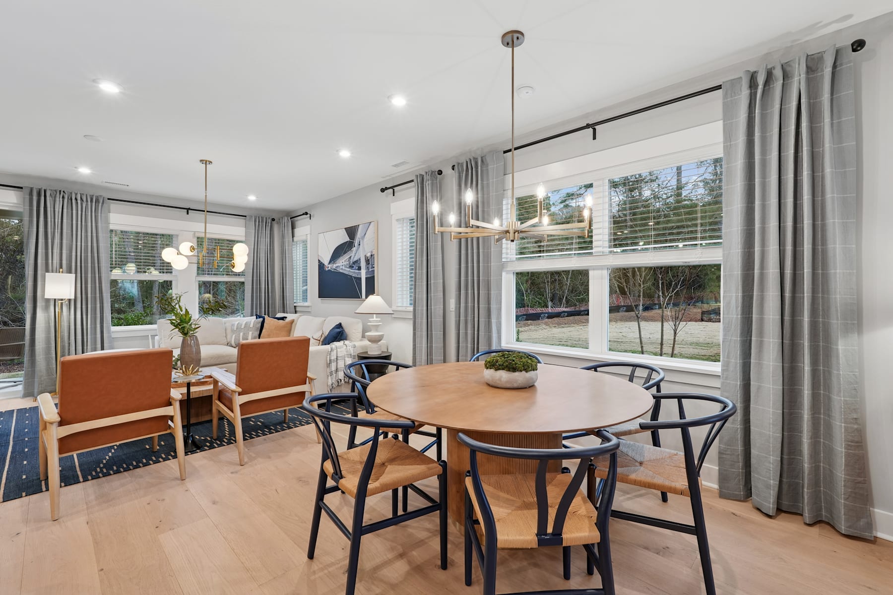 A modern and stylish dining area with a wooden table and chairs, surrounded by large windows overlooking a scenic outdoor view.