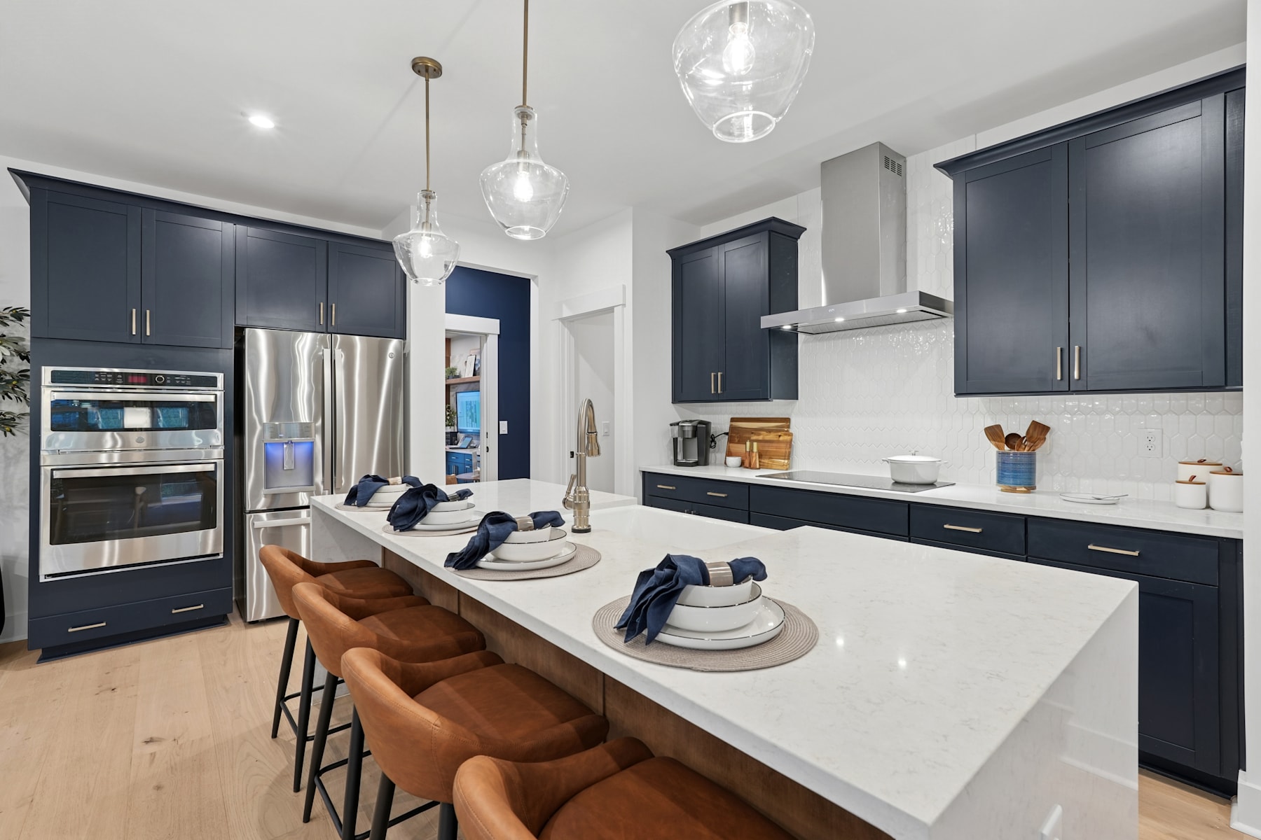 A modern, well-equipped kitchen with dark cabinets, white countertops, and pendant lighting fixtures, featuring a central island with bar stools.