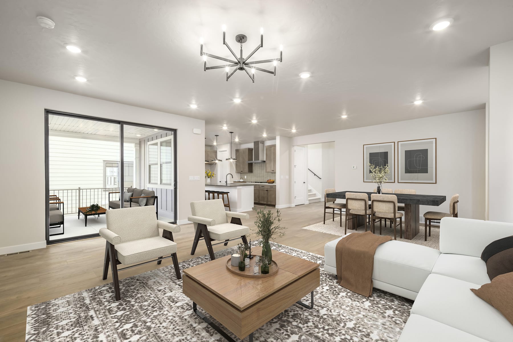 A modern and stylish living room with a large chandelier, white furniture, and a patterned rug in the foreground, leading to a kitchen and dining area in the background.