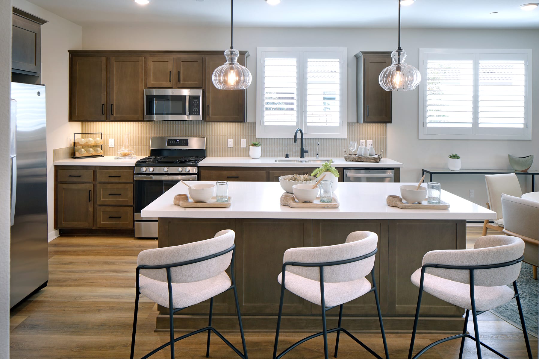 A modern and well-equipped kitchen with wooden cabinets, stainless steel appliances, and a central island with bar stools, illuminated by pendant lights.