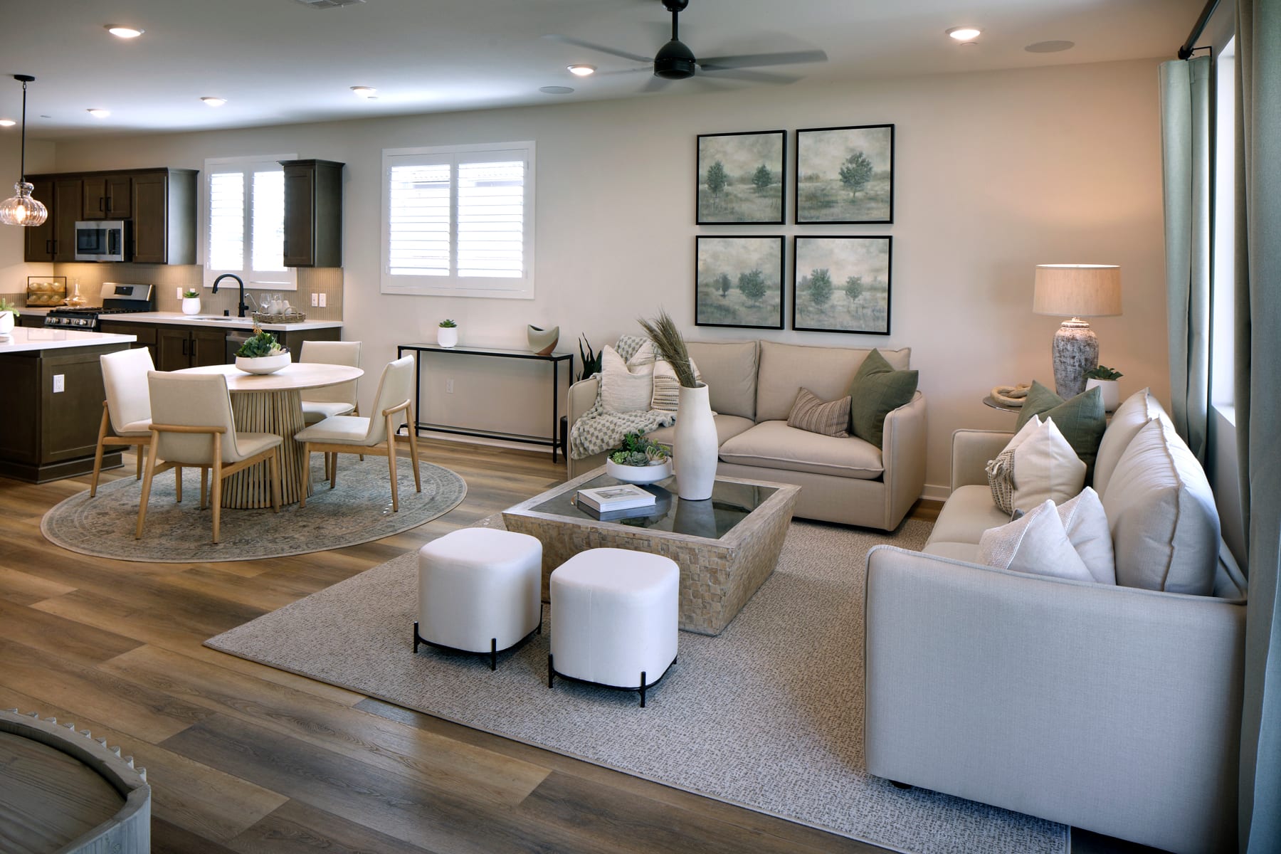 A cozy and modern living room with a kitchen visible in the background, featuring neutral-toned furniture, artwork on the walls, and a rug on the hardwood floor.