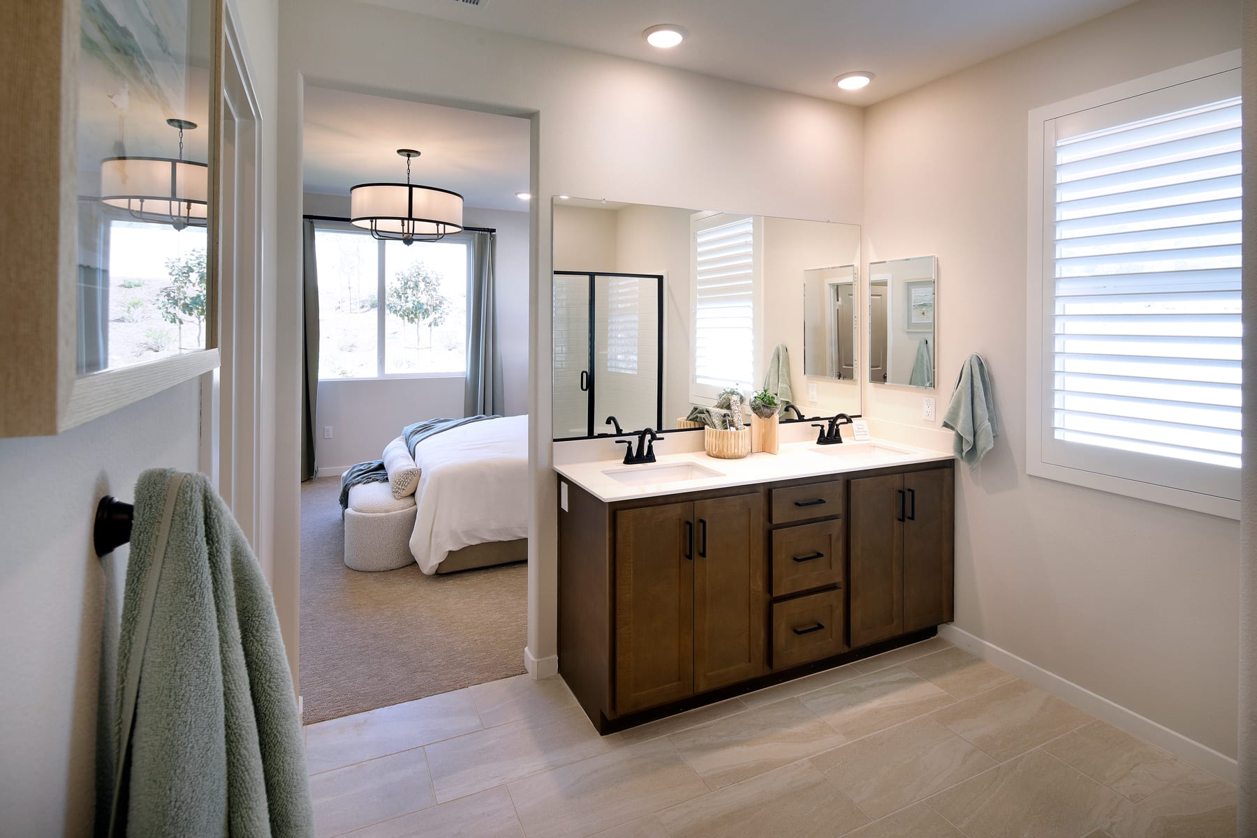 A spacious and well-lit bathroom with a wooden vanity, a large mirror, and a bedroom visible in the background.