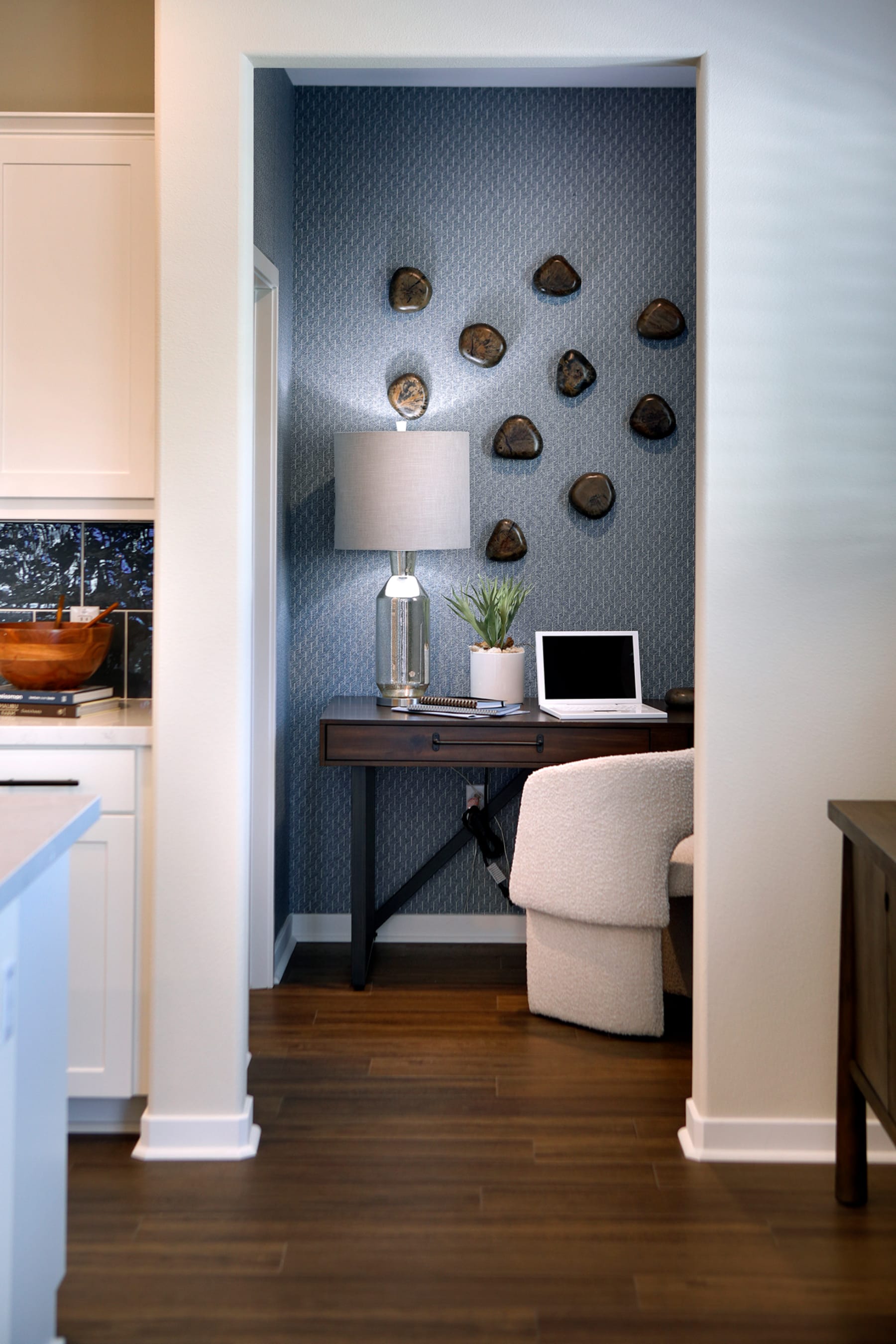 A cozy home office nook with a wooden desk, a lamp, and a potted plant, set against a wall adorned with decorative rock formations.
