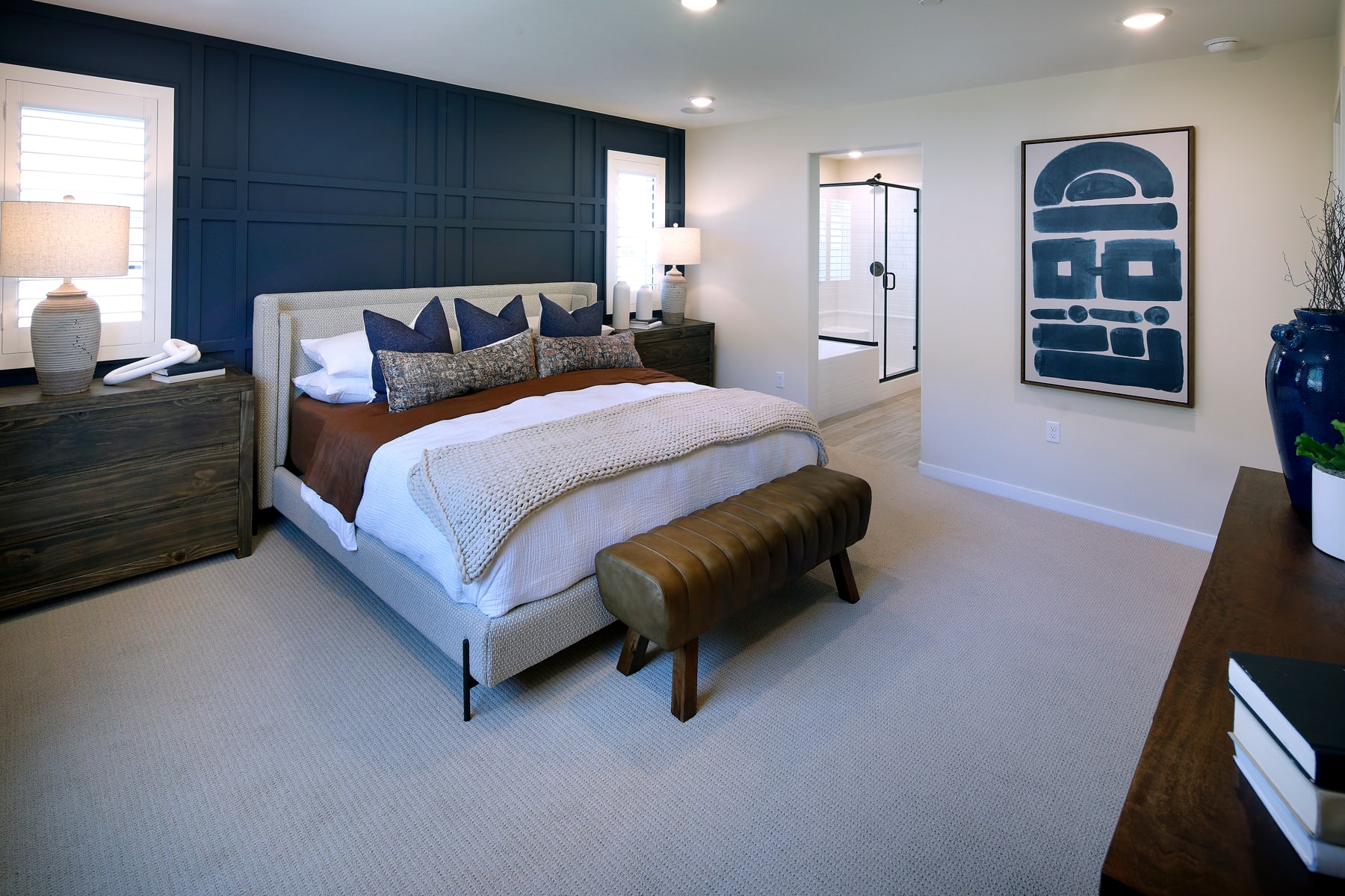 A modern and stylish bedroom with a navy blue accent wall, a wooden dresser, and a large abstract artwork on the wall.
