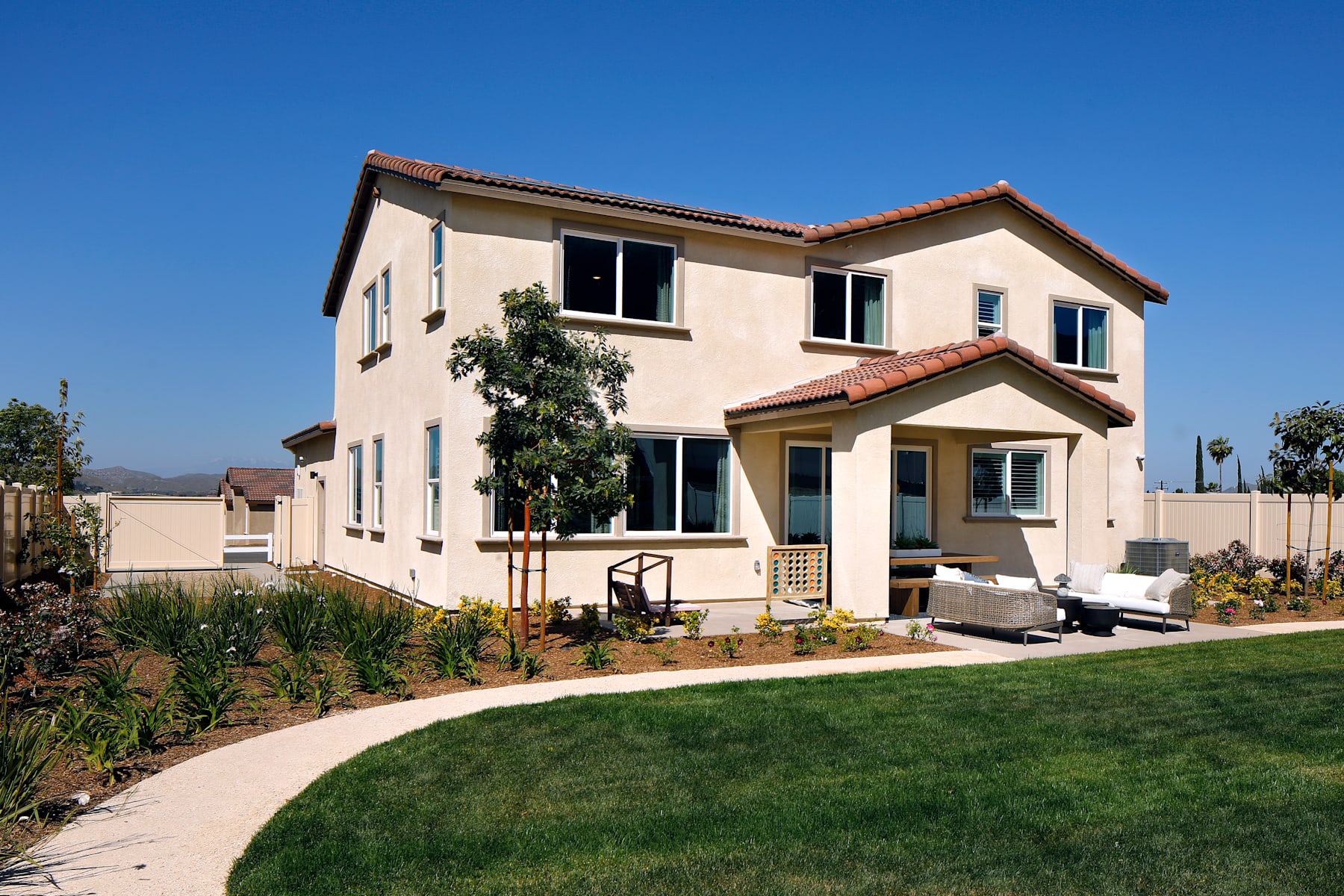 A two-story residential house with a tiled roof, surrounded by a well-maintained lawn and landscaping, set against a clear blue sky.