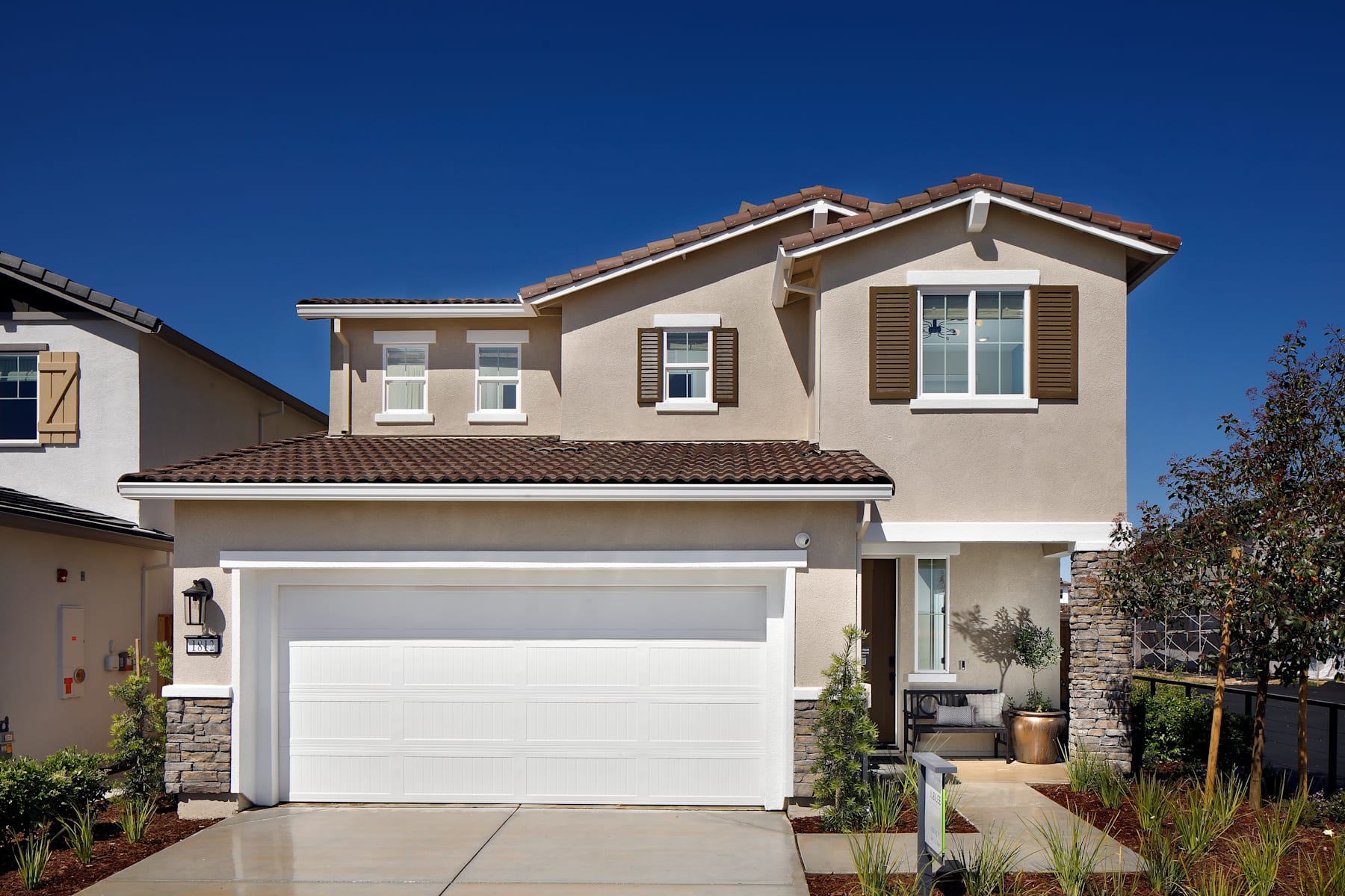 A two-story residential house with a garage door, surrounded by landscaping and a clear blue sky in the background.