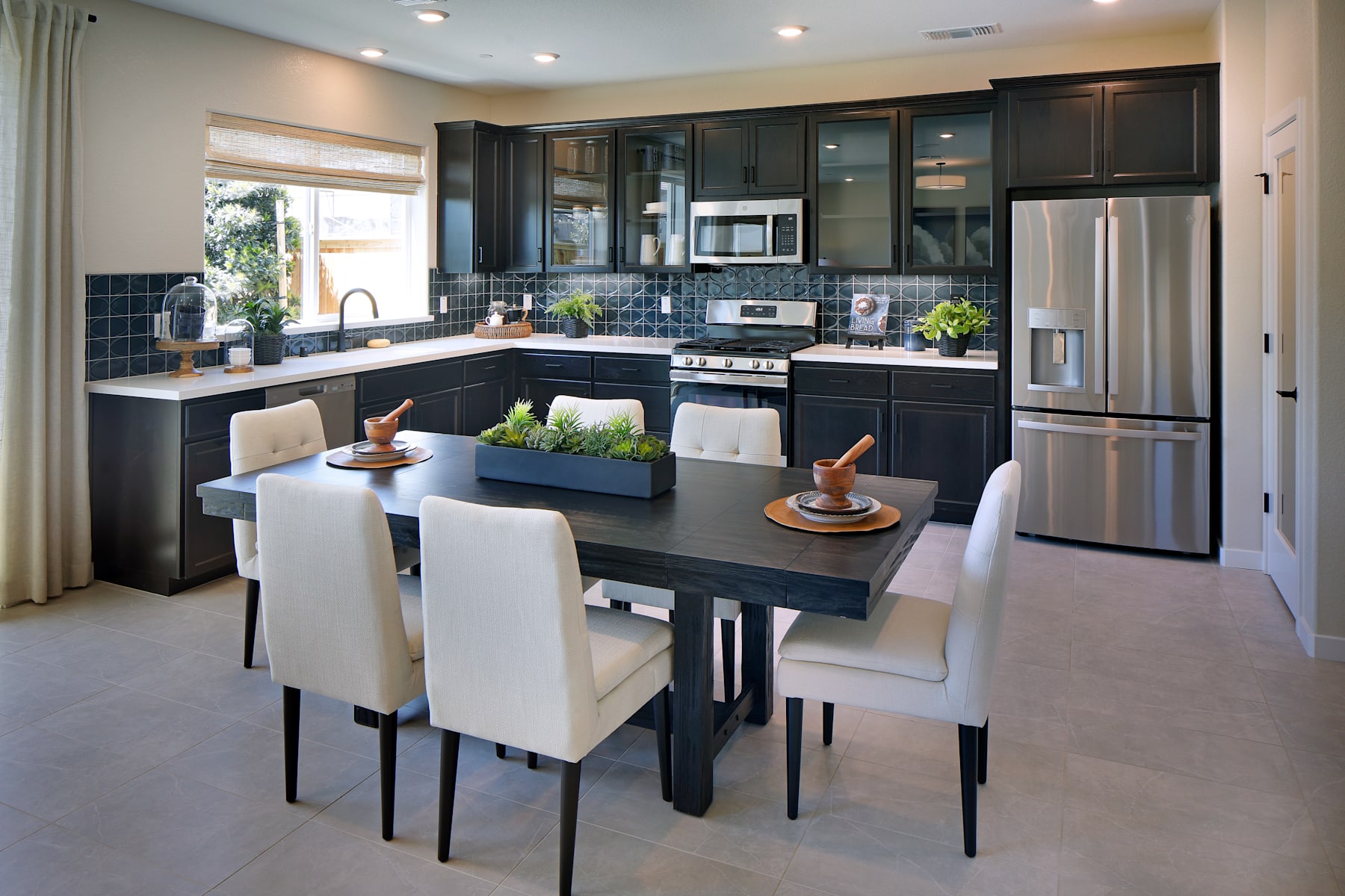 A modern and stylish kitchen with dark cabinets, stainless steel appliances, and a dining table with white chairs in the foreground.