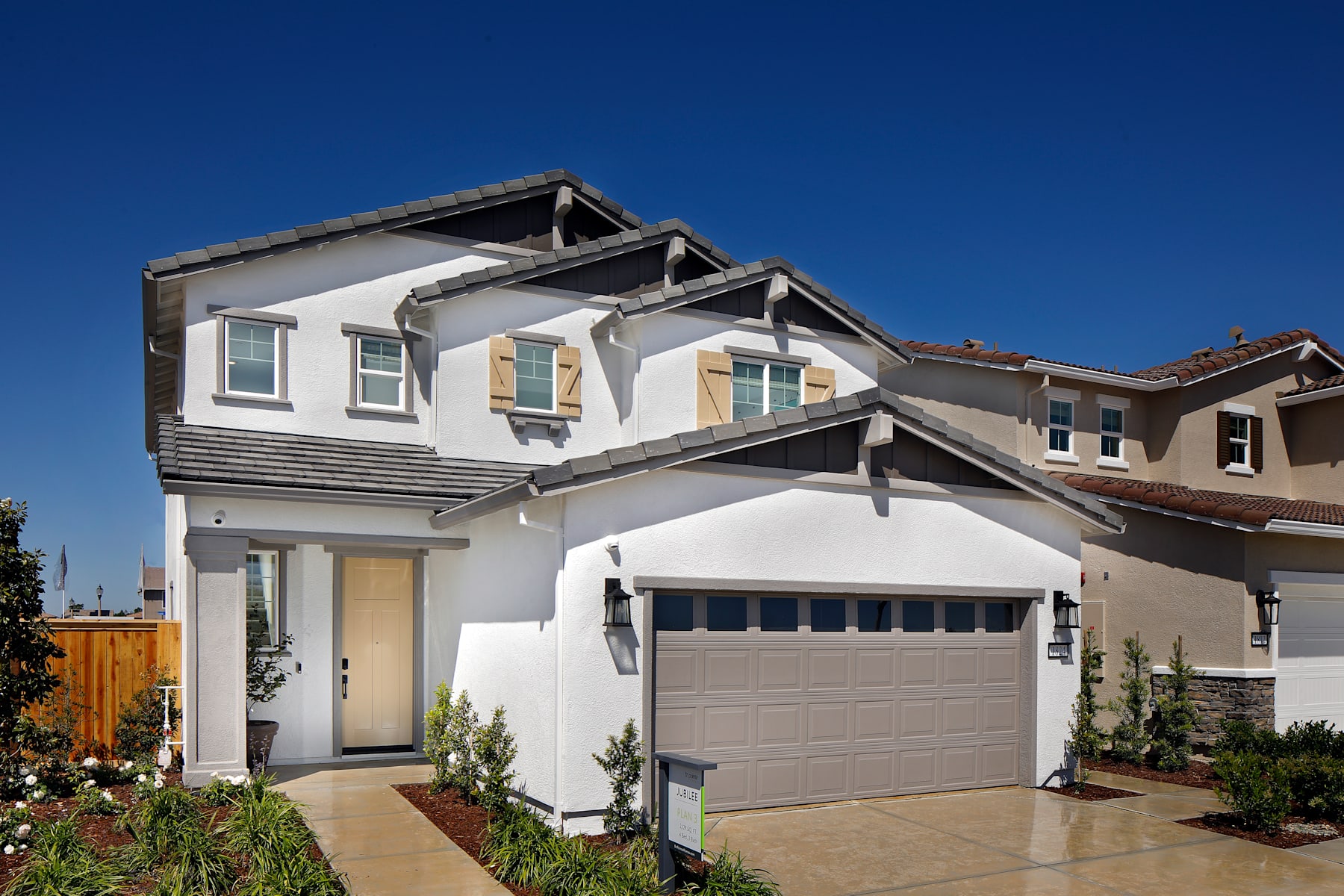 A two-story residential house with a garage, surrounded by a well-maintained lawn and landscaping, set against a clear blue sky.