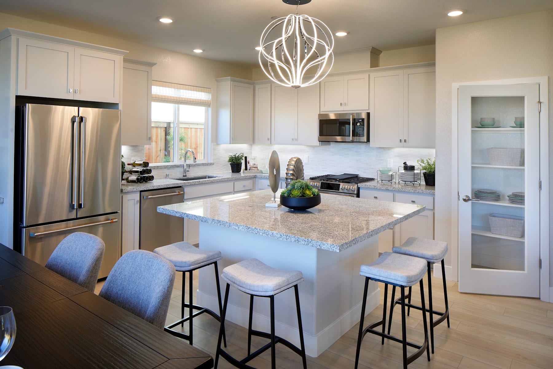 A modern, well-lit kitchen with white cabinets, stainless steel appliances, and a large central island with bar stools, complemented by a stylish pendant light fixture.