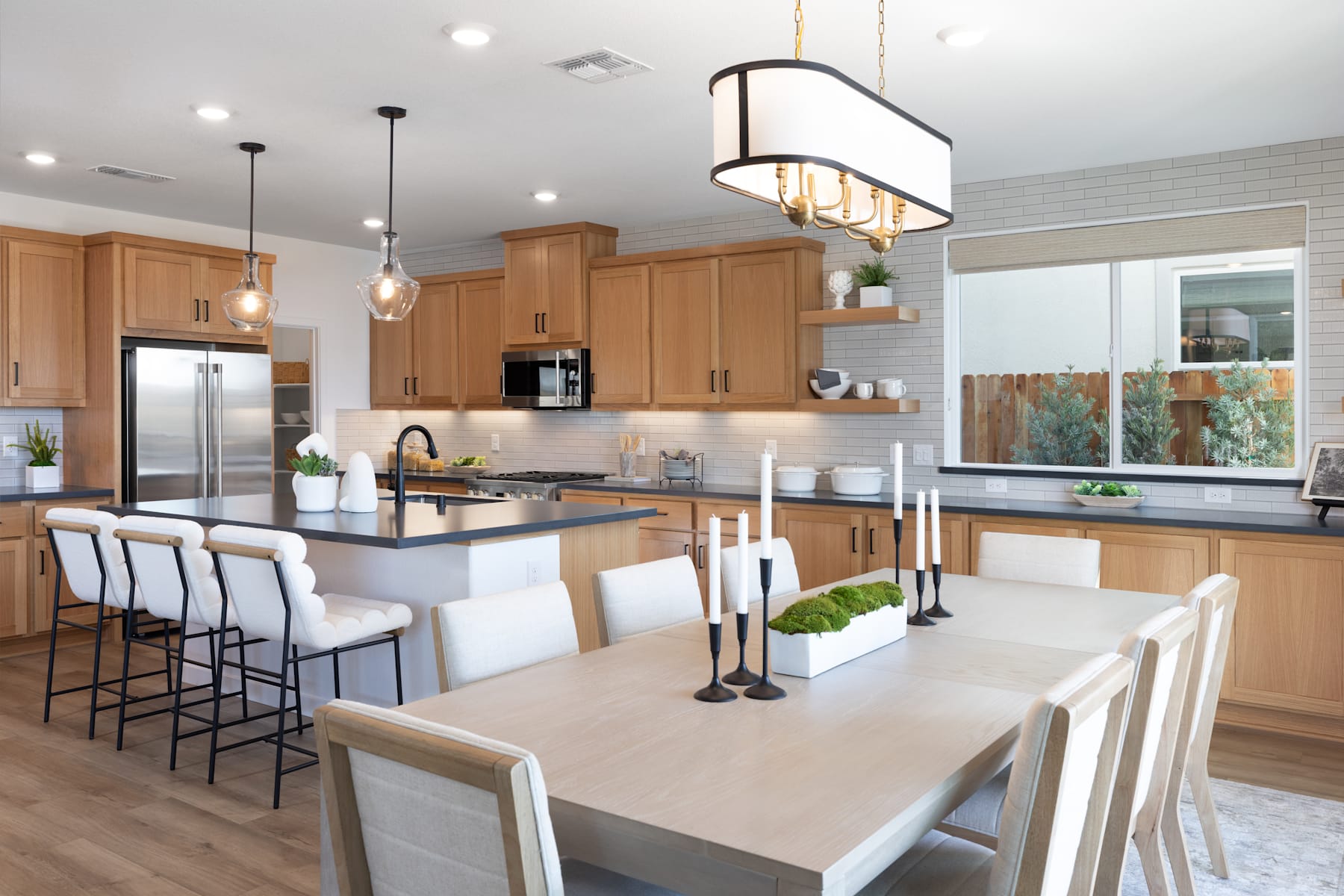 A modern and spacious kitchen with wooden cabinets, a large dining table, and a central island with bar stools, all illuminated by a stylish pendant light fixture.
