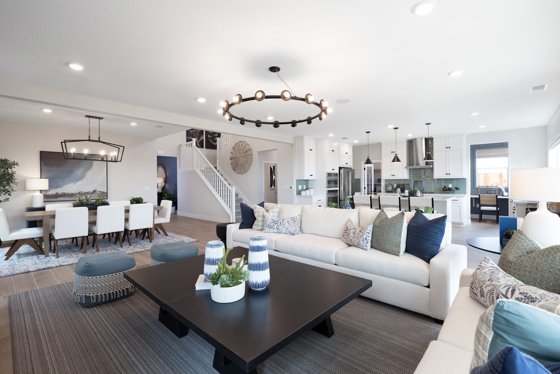 A spacious and well-designed living room with a large sofa, coffee table, and a chandelier overhead, surrounded by a dining area and an open-concept kitchen in the background.