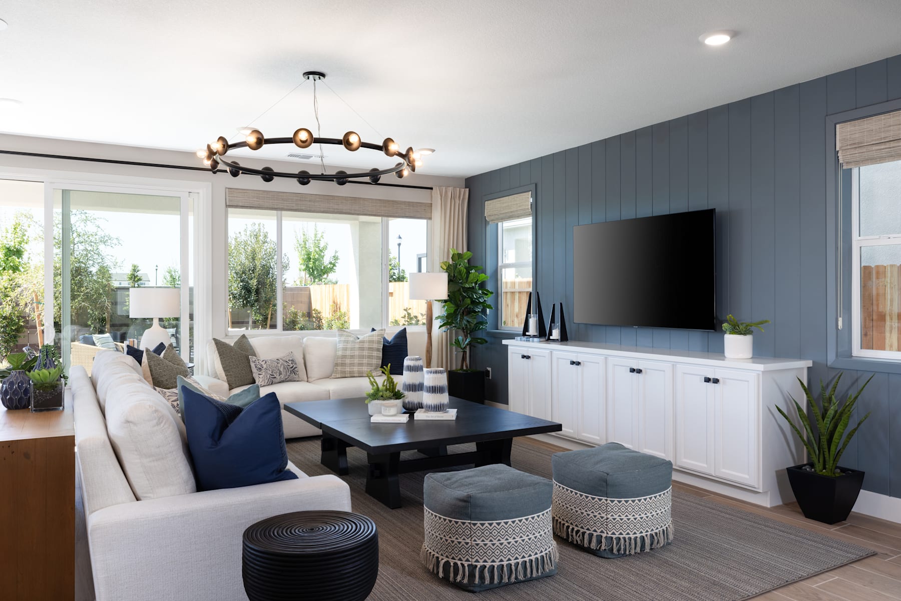 A cozy and modern living room with a large sofa, a coffee table, and a TV mounted on the wall, surrounded by large windows that let in natural light.