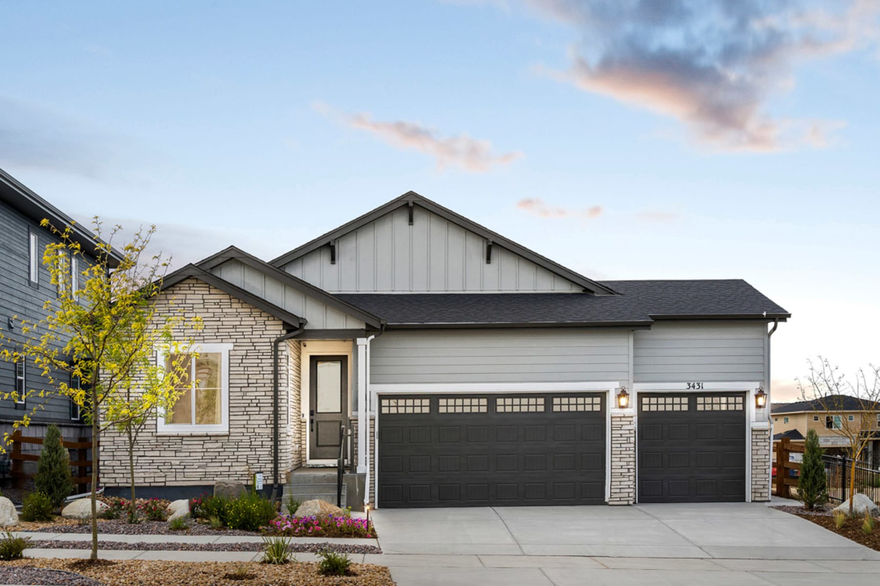 A modern two-story house with a stone facade, a garage, and a well-landscaped front yard against a backdrop of a partly cloudy sky.