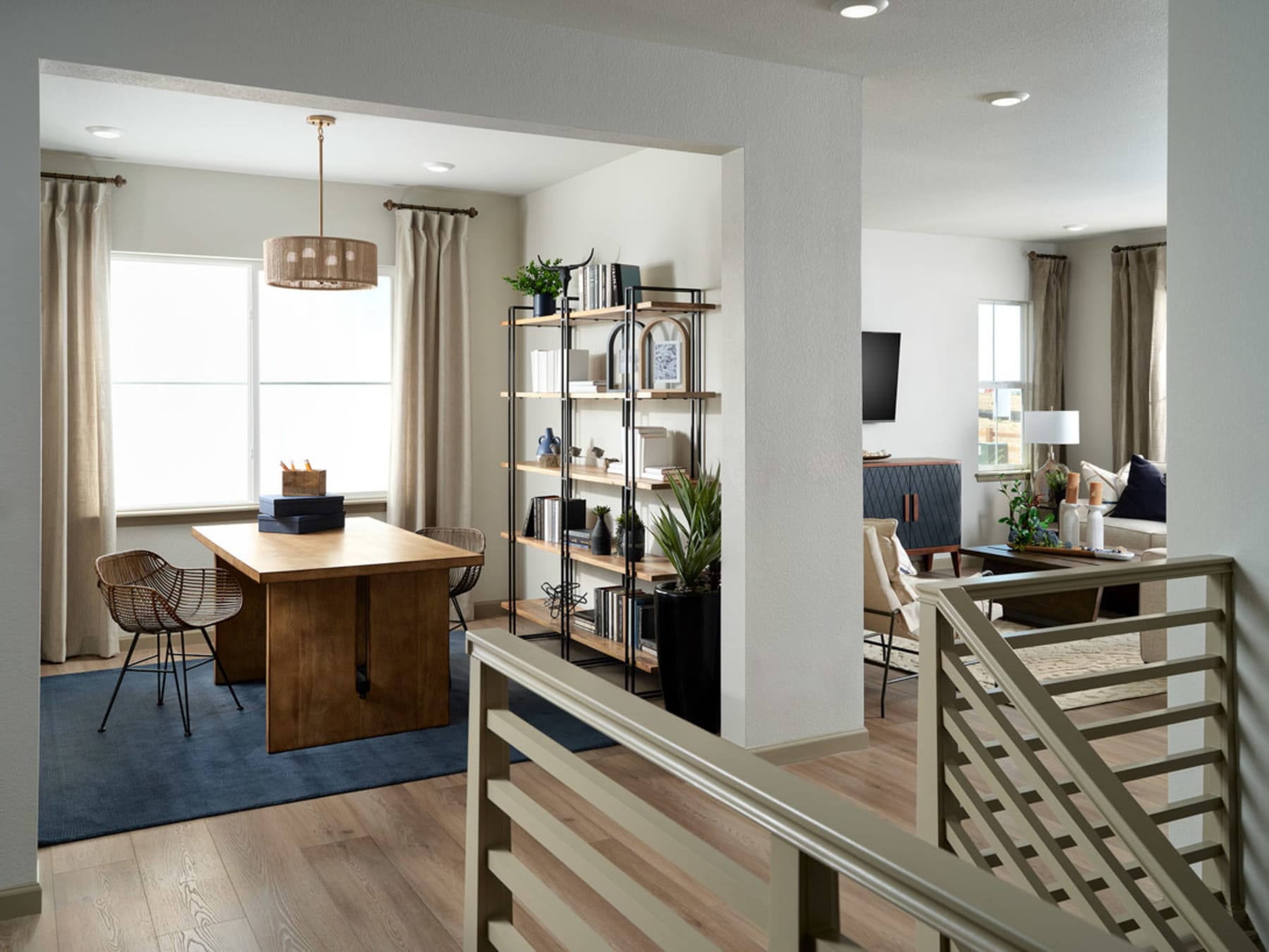 A modern and open-concept living space with a wooden dining table, shelving unit, and a staircase leading to an upper level.