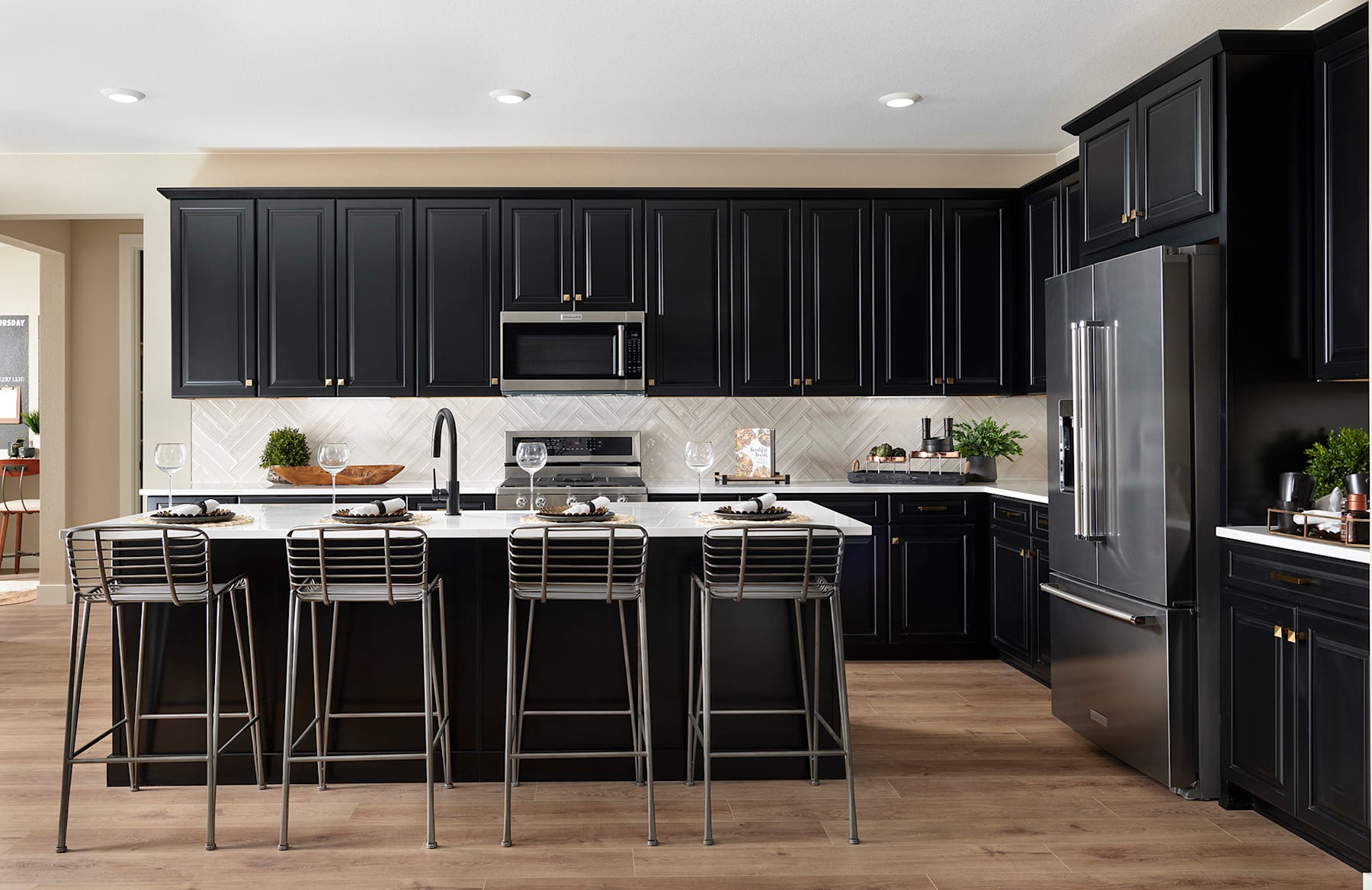 A modern and sleek kitchen with dark cabinets, stainless steel appliances, and a central island with bar stools, set against a light-colored backsplash and hardwood flooring.
