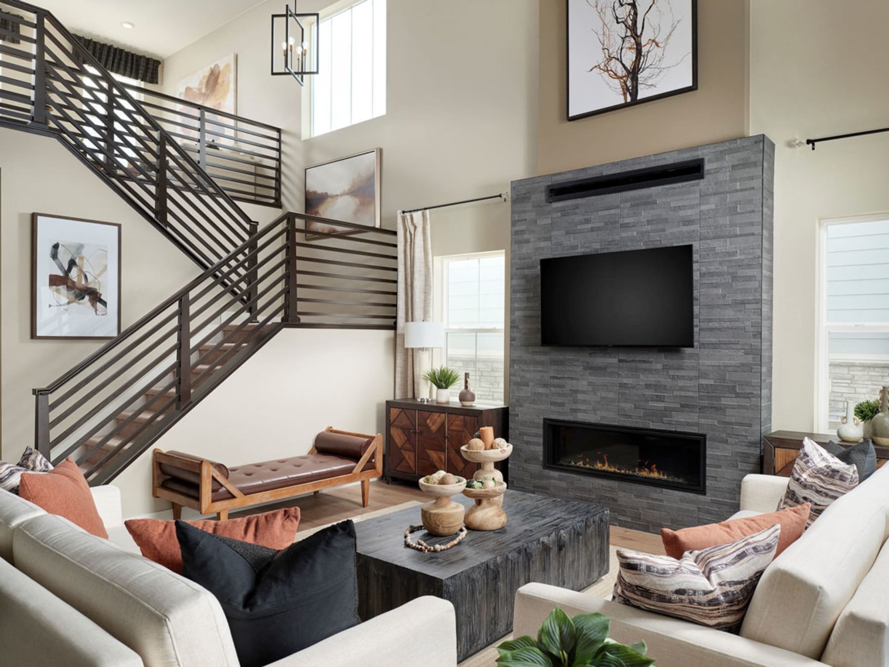 A modern and cozy living room with a fireplace, a TV, and a wooden staircase leading to an upper level, surrounded by comfortable furniture and decorative elements.