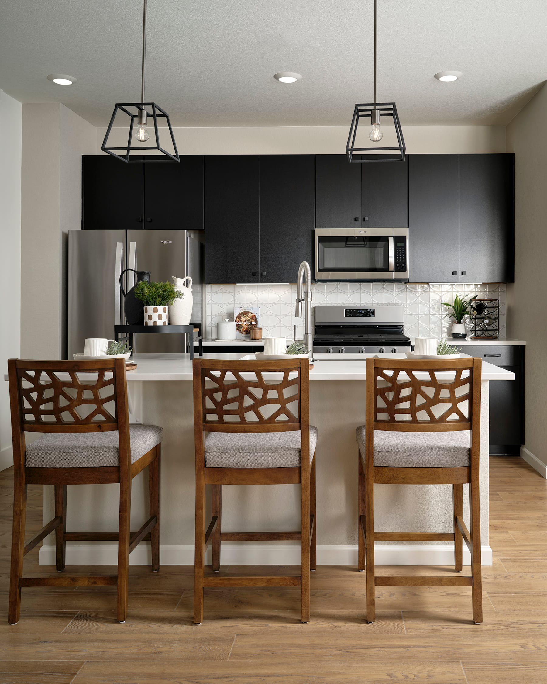 A modern kitchen with black cabinets, stainless steel appliances, and wooden bar stools in the foreground.