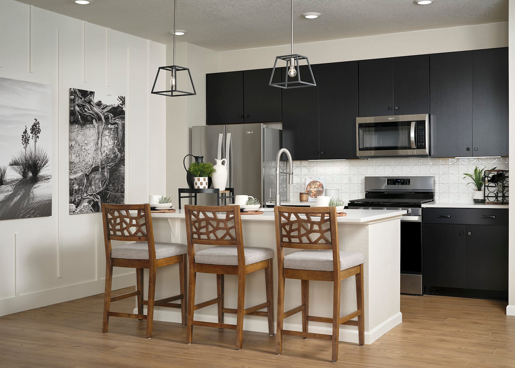A modern and stylish kitchen with a black accent wall, white cabinets, wooden bar stools, and a large refrigerator in the background.
