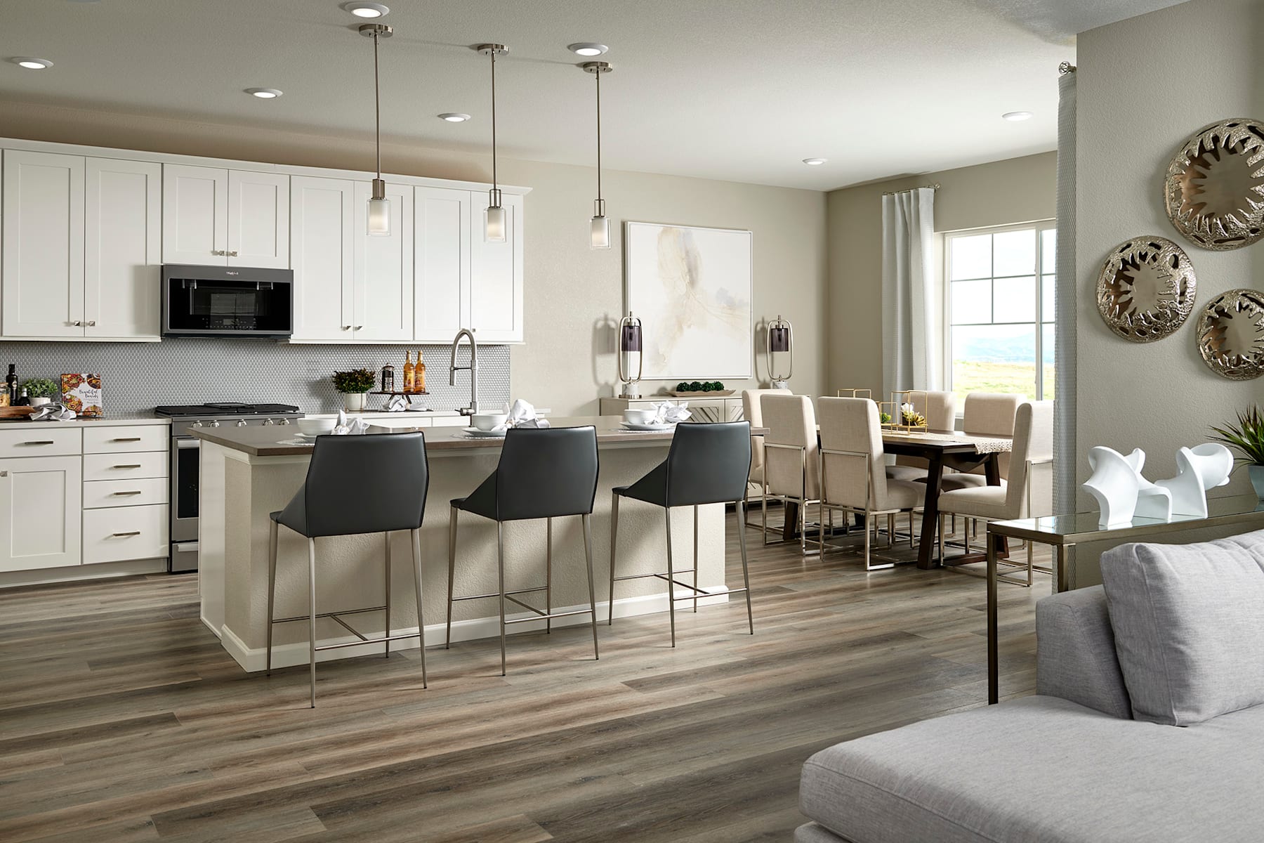 A modern and spacious kitchen with white cabinets, a large island with bar stools, and a dining area with a wooden table and chairs, all set against a neutral color scheme and accented with decorative wall pieces.