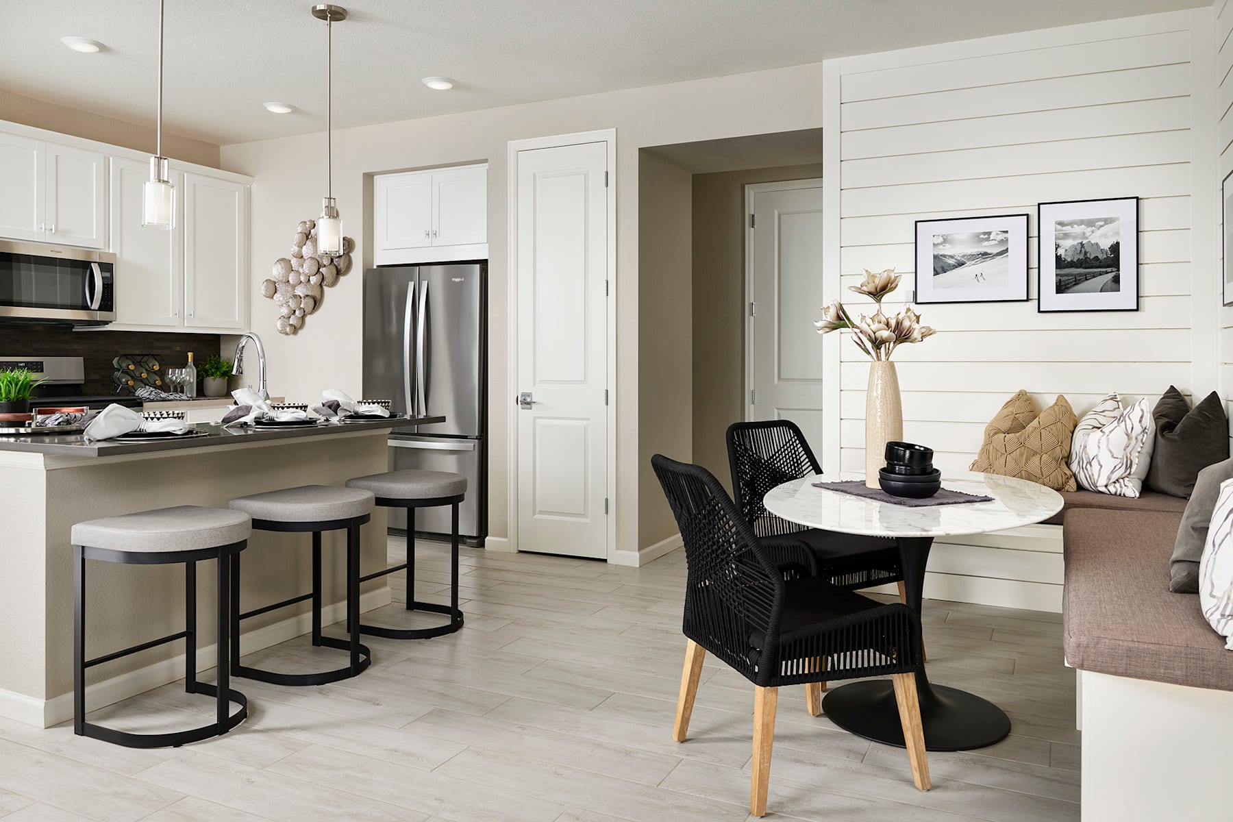 A modern and minimalist kitchen and dining area with white walls, stainless steel appliances, and a round dining table with black chairs.